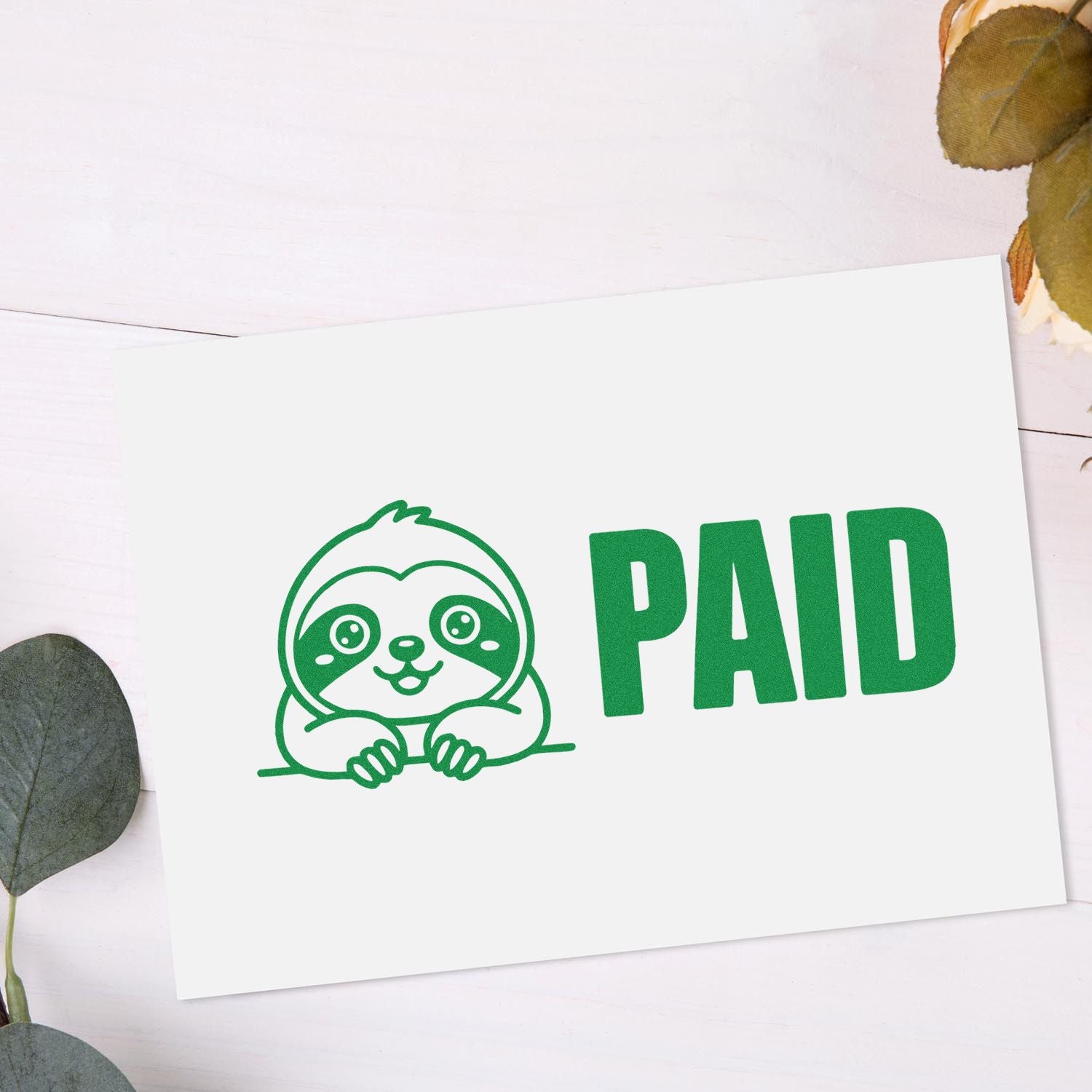 Green PAID stamp seal with cute sloth logo on white card, accented by muted leaves.