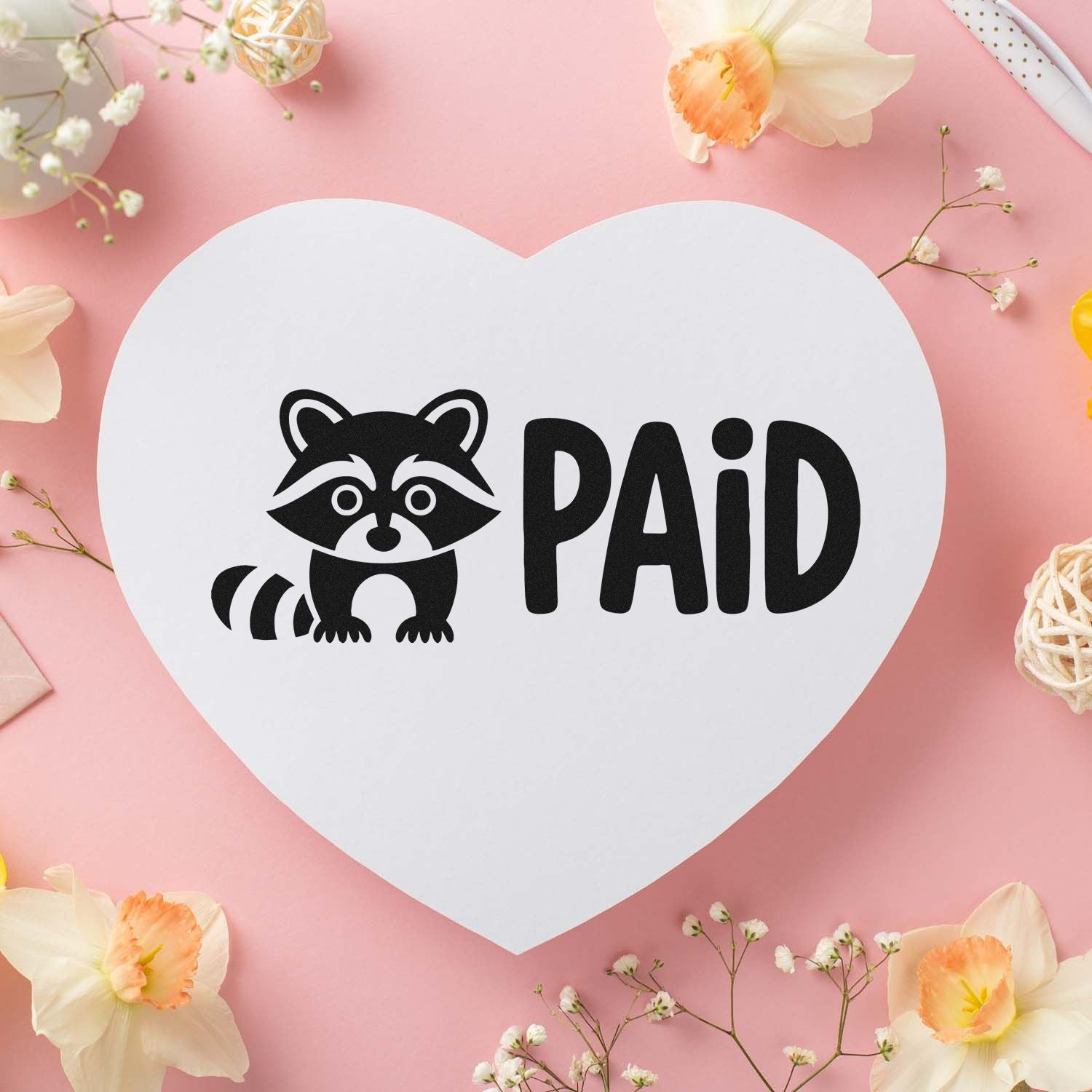 Black raccoon PAID stamp on a white heart-shaped seal card, set against a pink floral background.