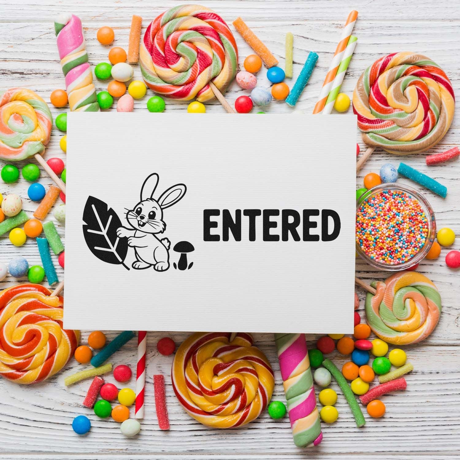 Black ENTERED stamp and bunny seal logo on white card, surrounded by colorful lollipops and candy.