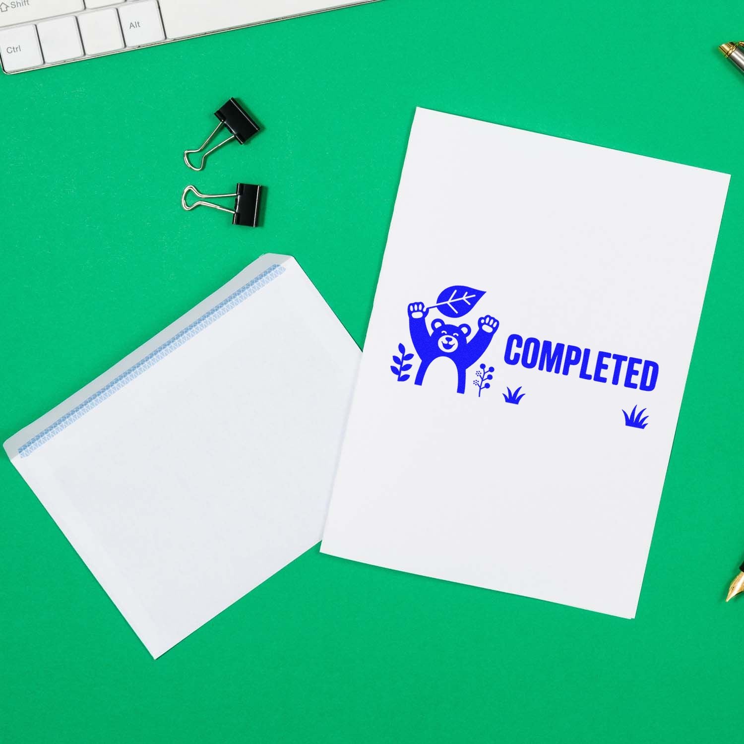 Blue bear COMPLETED stamp seal on white papers beside a sealed envelope, black binder clips, on a green background.
