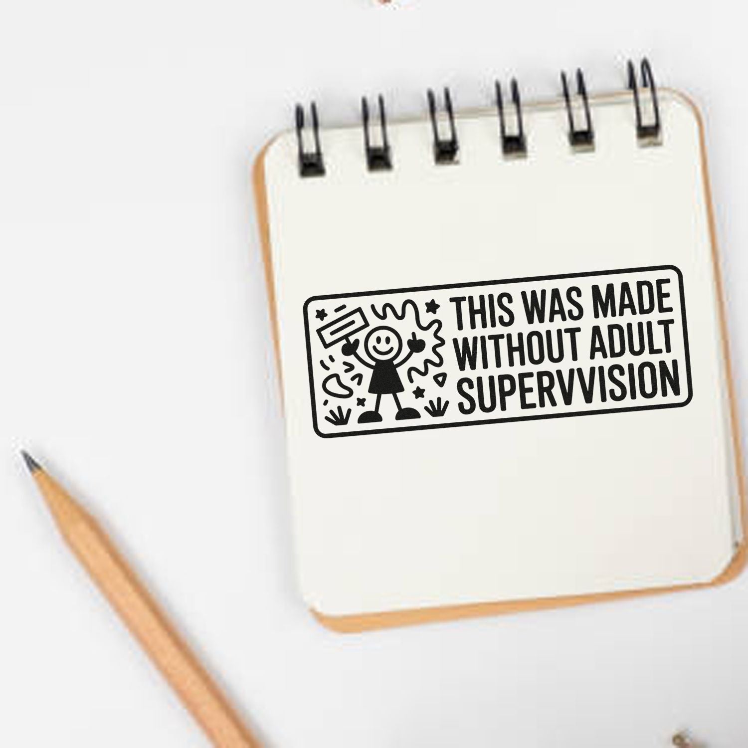Black stamp seal reading This Was Made Without Adult Supervision on a cream spiral notebook beside a wooden pencil.