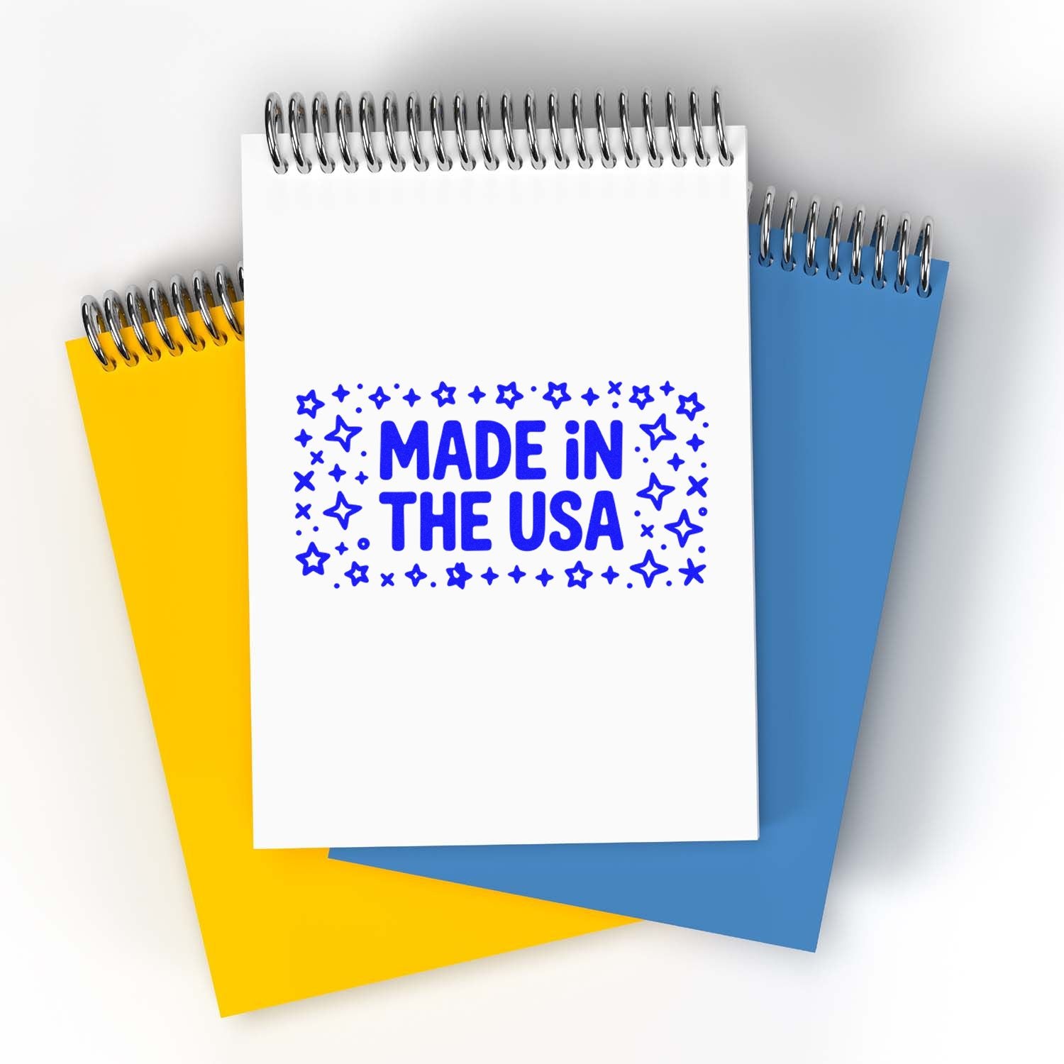 Spiral notebook stamp and seal design with blue Made in the USA text, star border, on white page over yellow and blue pads.