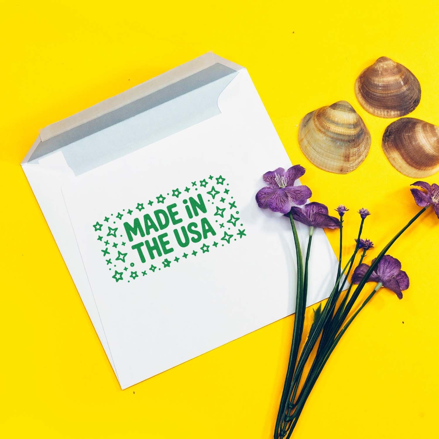 White mailer with green MADE IN THE USA stamp, bright yellow background, purple flowers, and seashell seal samples.