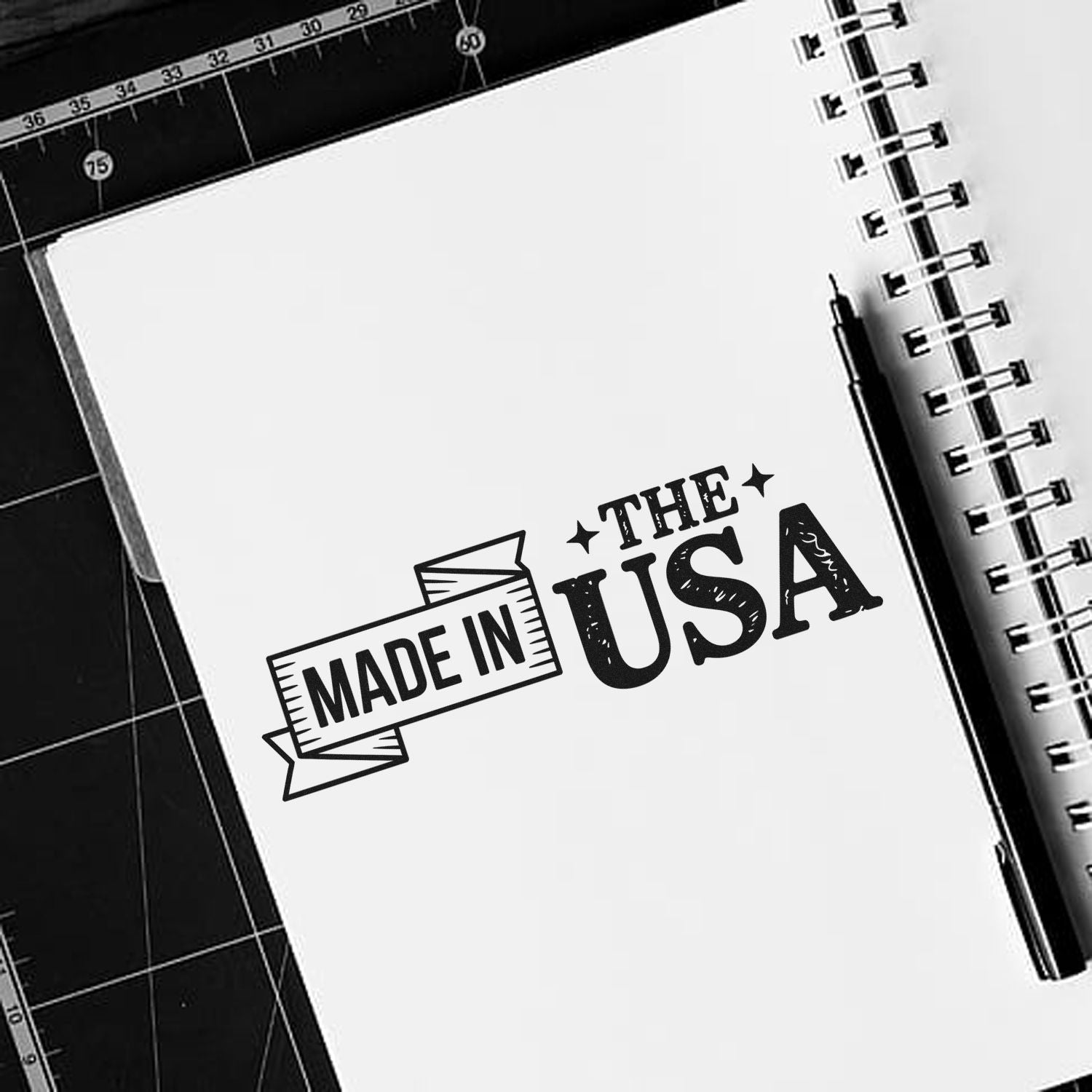 Black Made in the USA custom stamp on a white spiral notebook, with pen and black cutting mat.