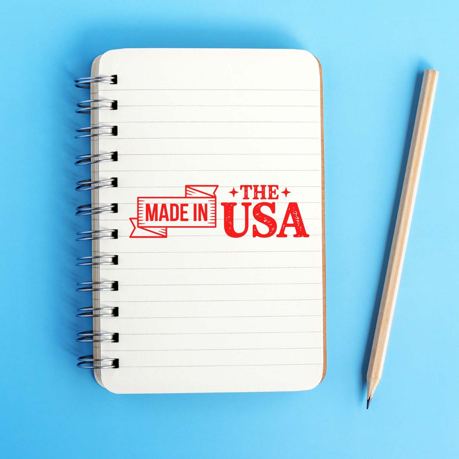 Red Made in USA rubber stamp on white spiral notebook, with pencil, against bright blue background.