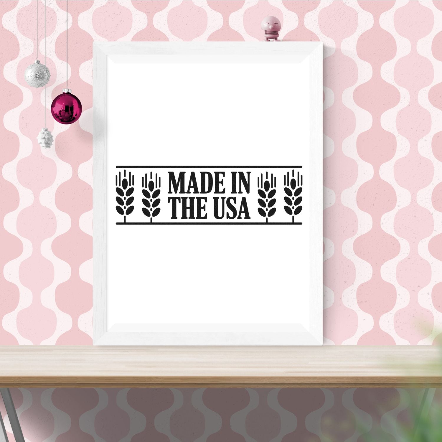 Black Made in the USA rubber stamp seal on a white frame, set against pink patterned wallpaper with hanging ornaments.