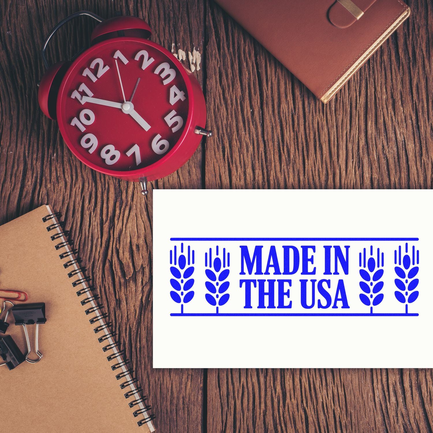 Blue Made in the USA seal stamp with a red alarm clock, notebook, and leather planner on a wood desk.