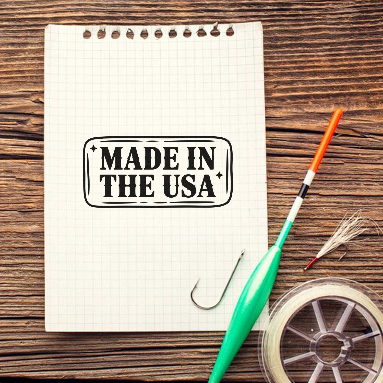 Black Made in the USA stamp seal on grid notebook, with green craft tool and clear tape roll on wood background.