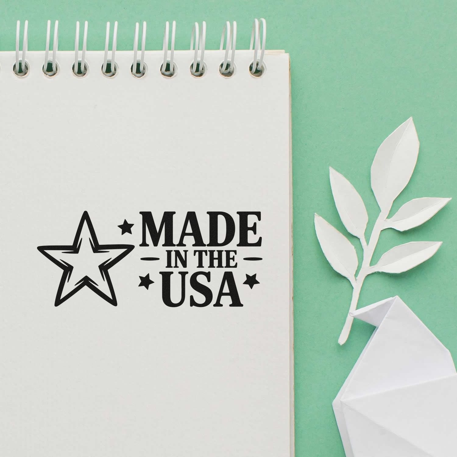 Black Made in the USA rubber stamp on a white spiral notebook, with white paper leaf seal pieces on a mint green background.