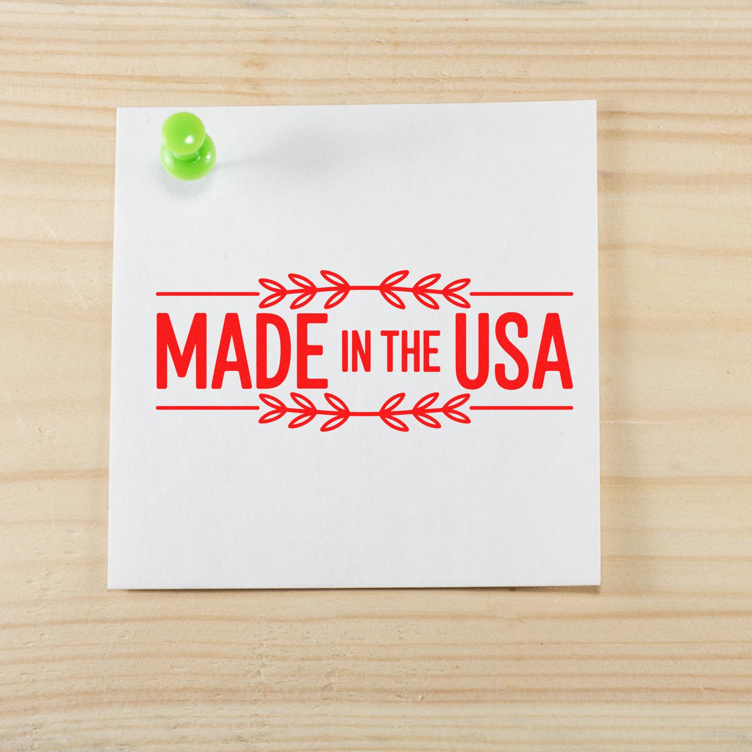 Red Made in the USA stamp seal on white paper, pinned with a green pushpin on a light wood background.