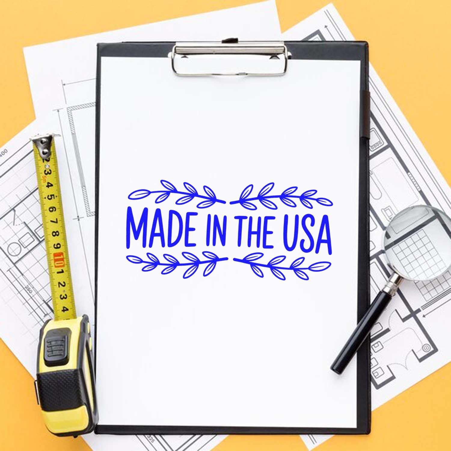 Blue Made in the USA stamp seal on a white clipboard, with a yellow tape measure and blueprint plans on an orange background.