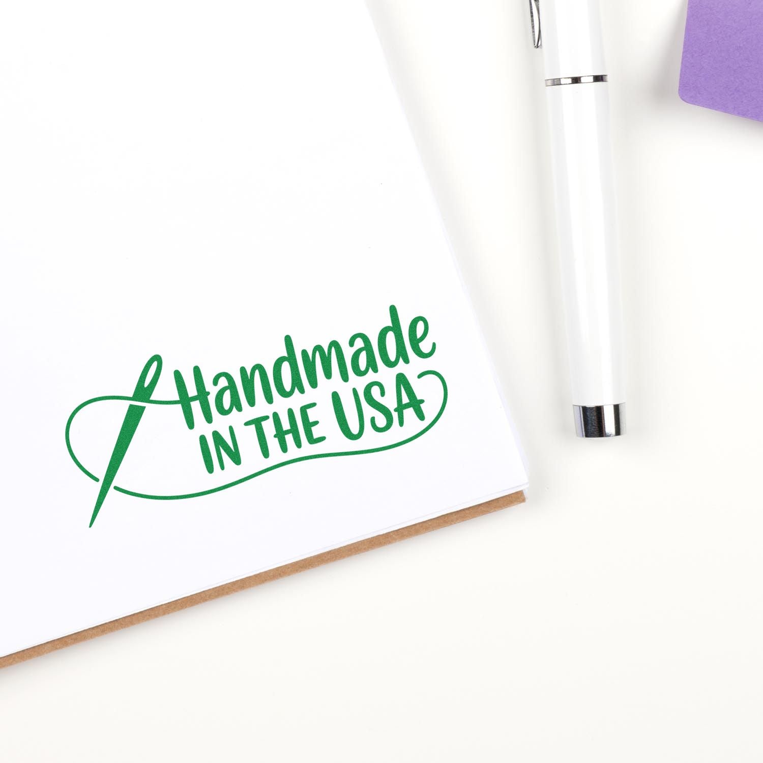 Green Handmade in the USA stamp seal on white paper with a white pen and purple accent.