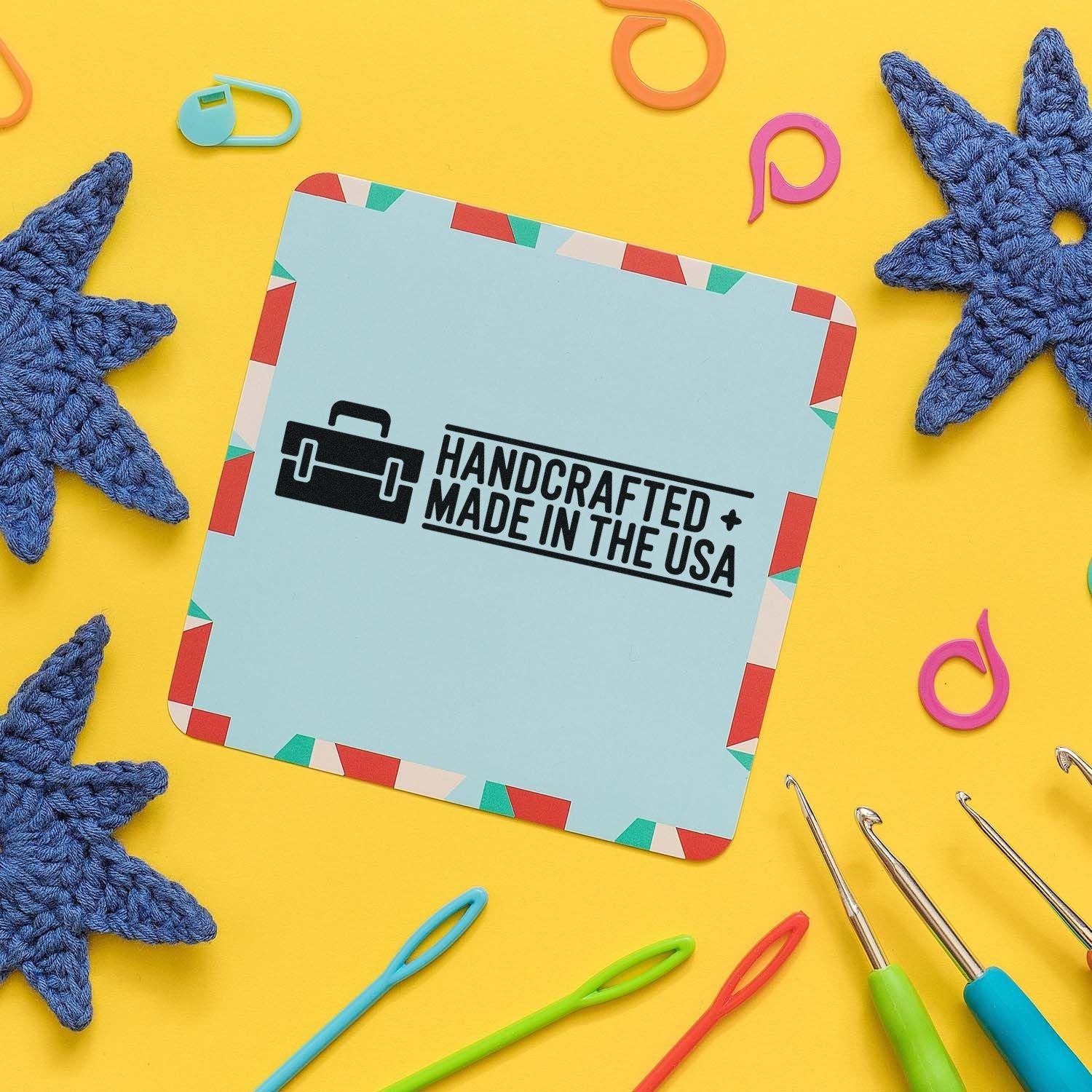 Blue handcrafted made in the USA stamp and seal card with colorful border on yellow background, surrounded by crochet stars and hooks.