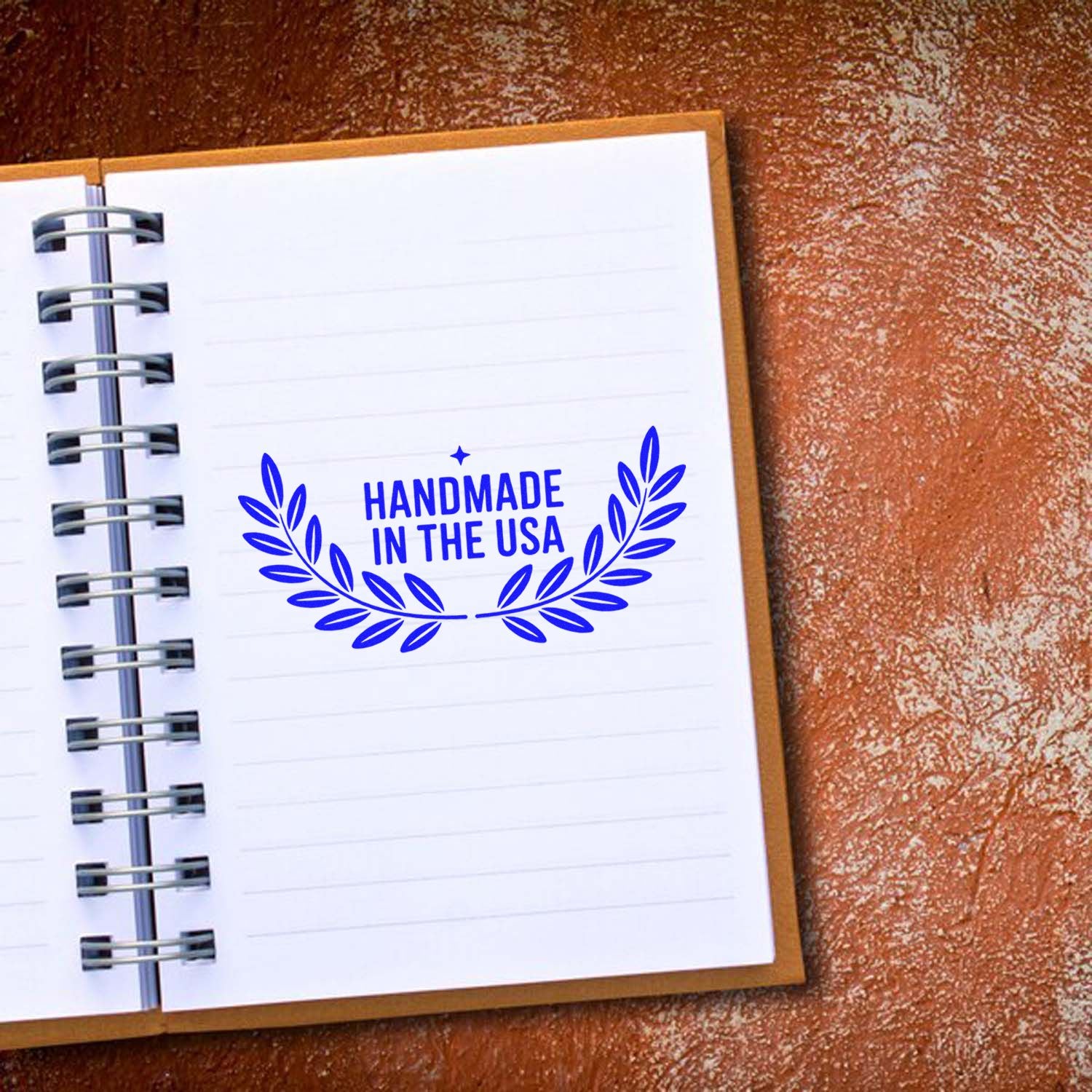 Blue Handmade in the USA stamp seal with laurel wreath on a white spiral notebook page, set on a brown textured background.