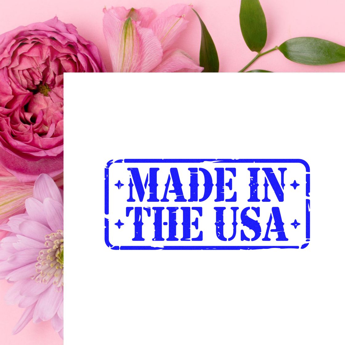 Blue Made in the USA rubber stamp seal on white, framed by pink flowers and green leaves.