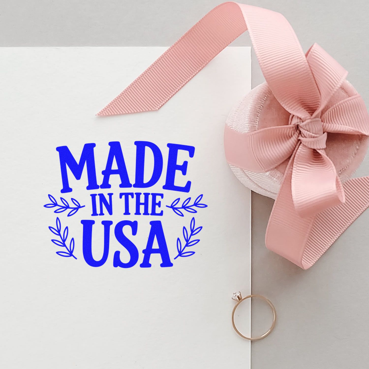 White card with blue Made in the USA stamp and pink ribbon bow seal, plus a gold ring.