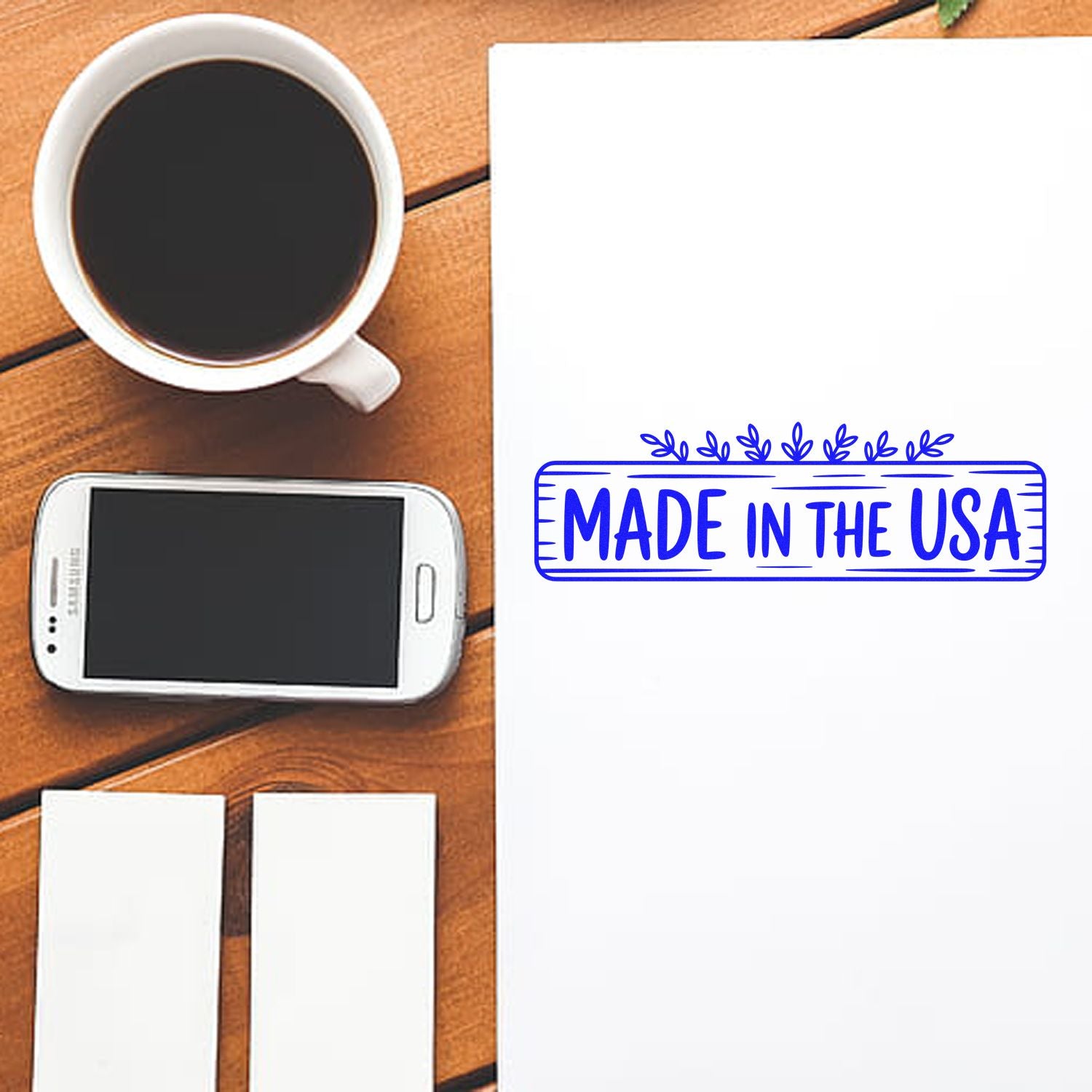 Blue Made in the USA stamp seal on white paper beside a coffee cup, smartphone, and blank cards on a wood table.