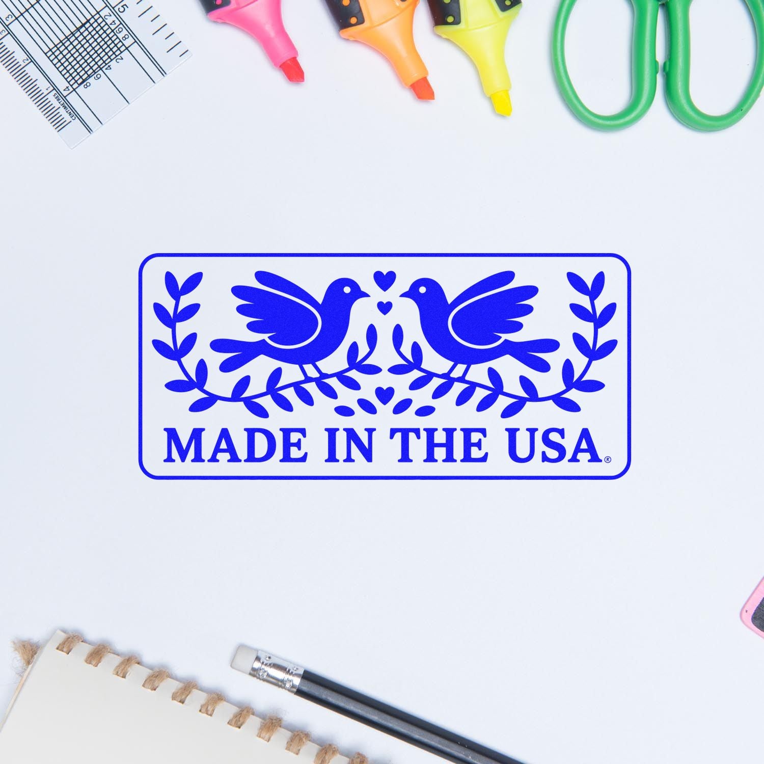 Blue Made in the USA rubber stamp with birds and laurel, surrounded by colorful stamp and seal tools on white.