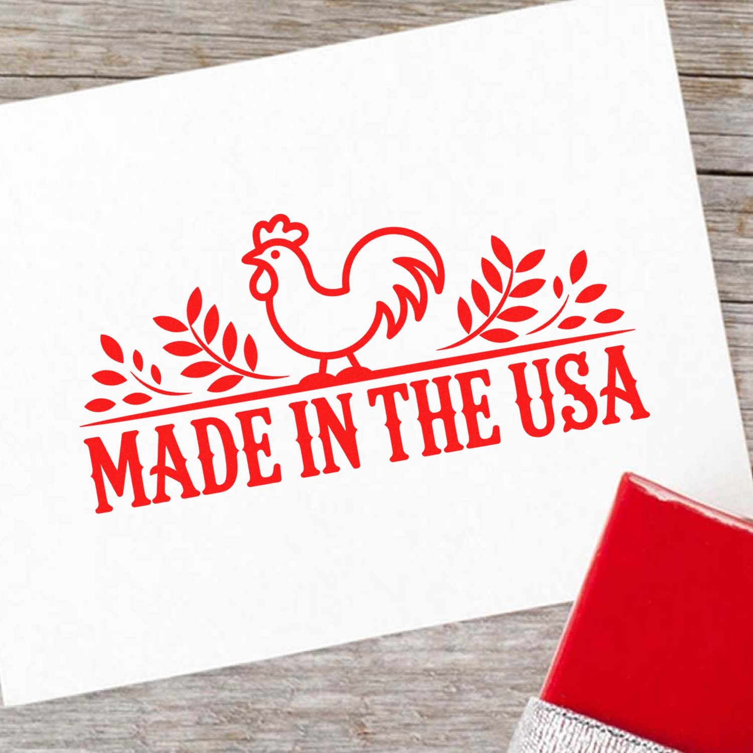 Red Made in the USA rooster stamp seal on white paper, with a matching red stamp tool on a gray wood background.