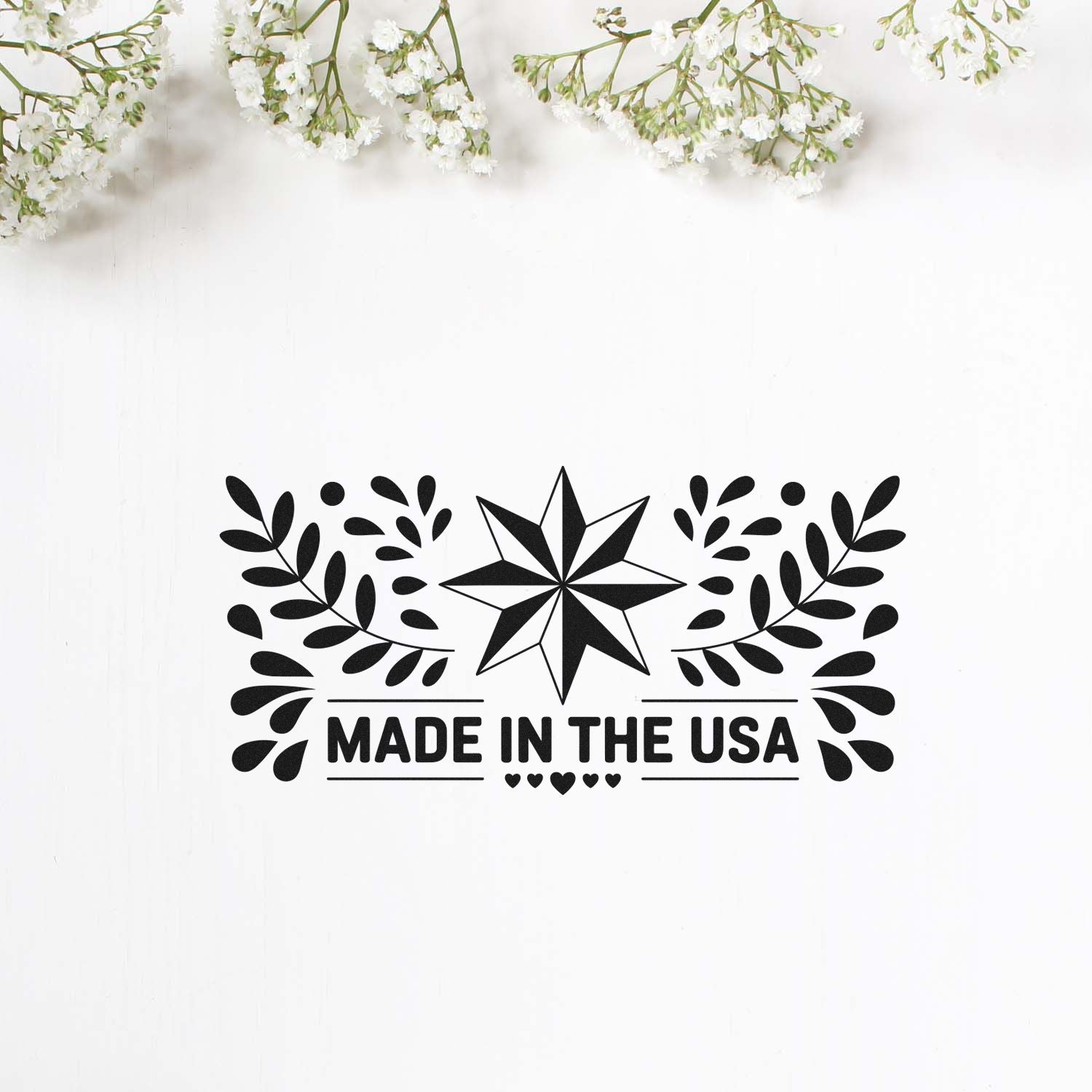 Black Made in the USA stamp and seal with star, leaf wreath, and small hearts on a white background with white flowers above.