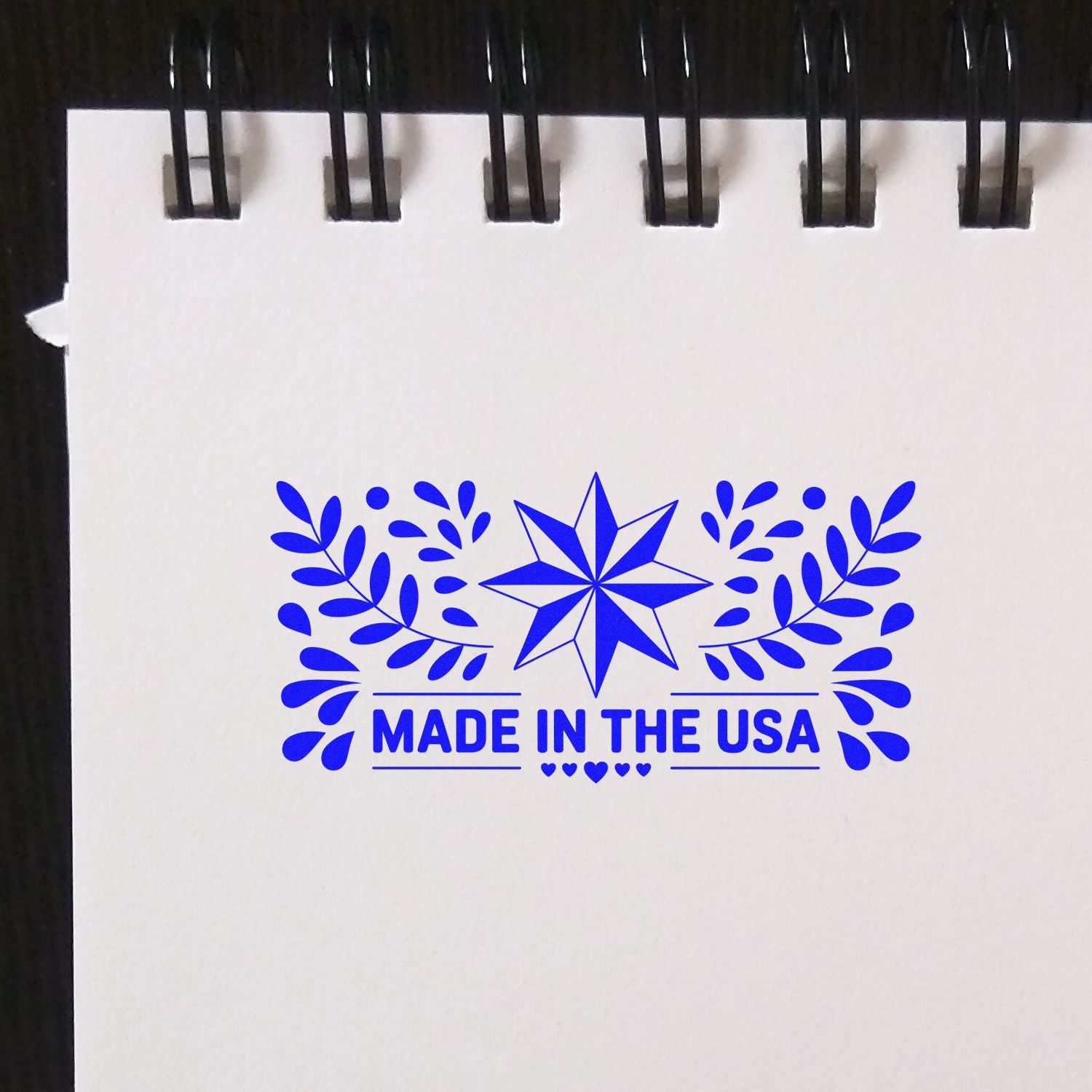Blue Made in the USA stamp seal with star, laurel leaves, and hearts on a white spiral notebook page.
