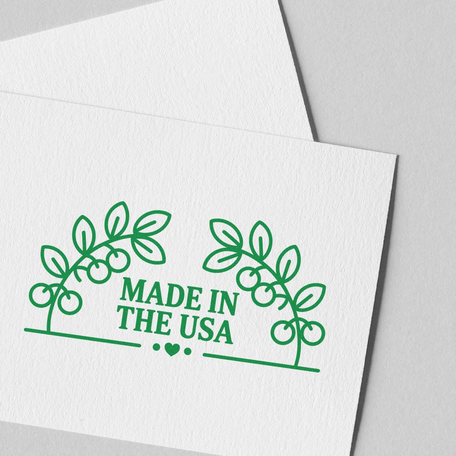 Green Made in the USA stamp seal with leafy wreath and heart on white textured paper