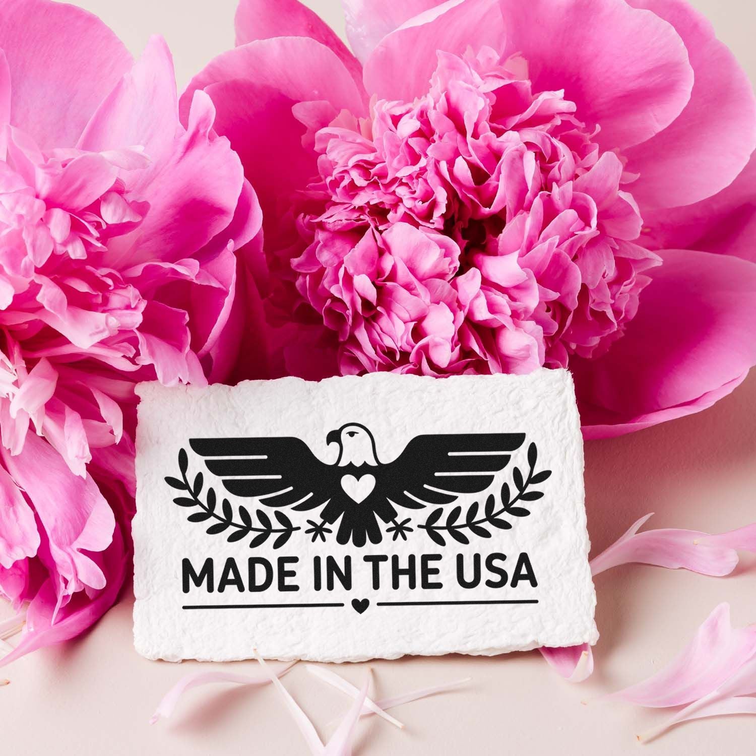 White stamp seal product with black eagle, heart, and MADE IN THE USA text on bright pink peonies.