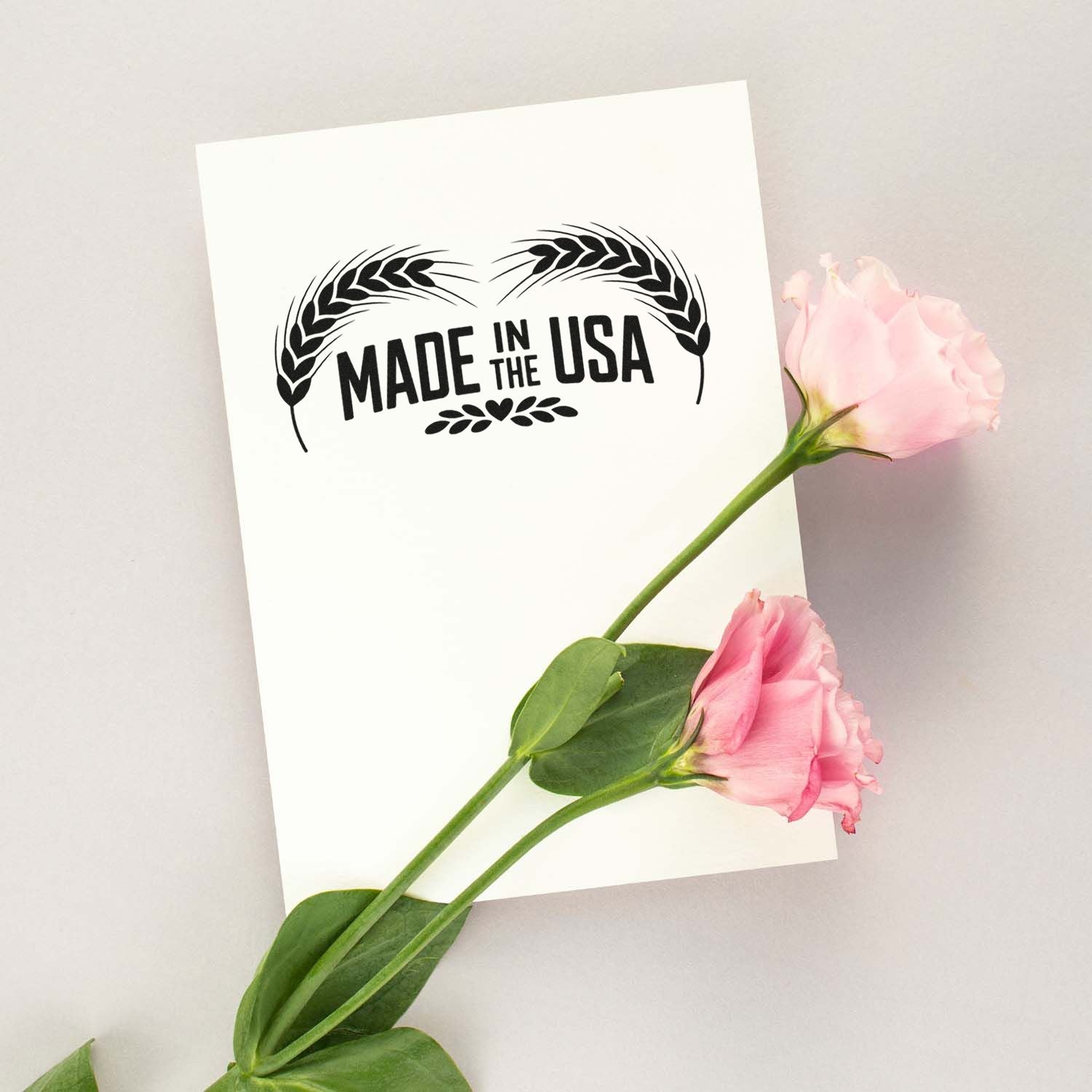 Black Made in the USA stamp seal with wheat motif on white cardstock, styled with pink roses and green stems.
