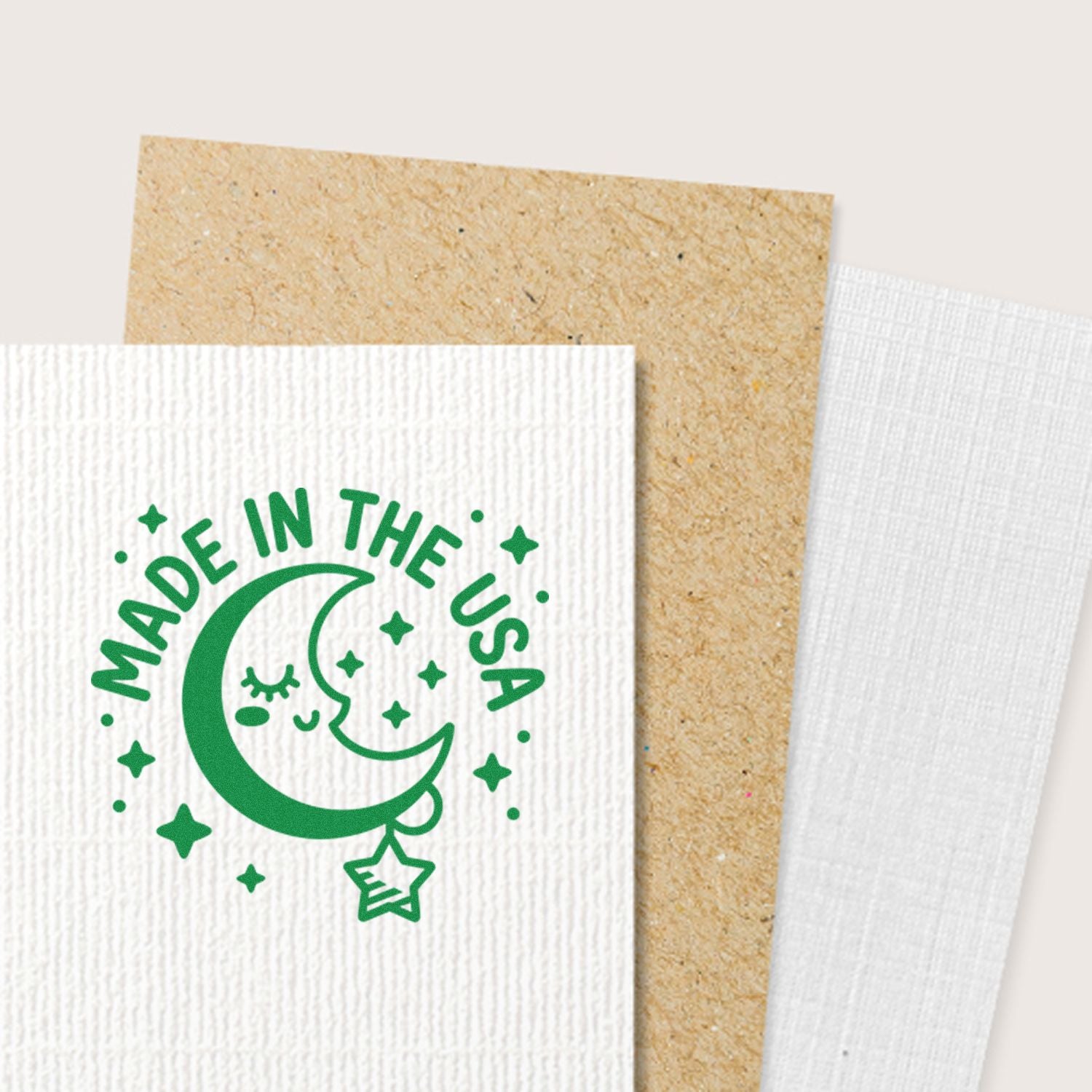 Green Made in the USA moon-and-stars stamp and seal on white textured cardstock with tan and white sample papers