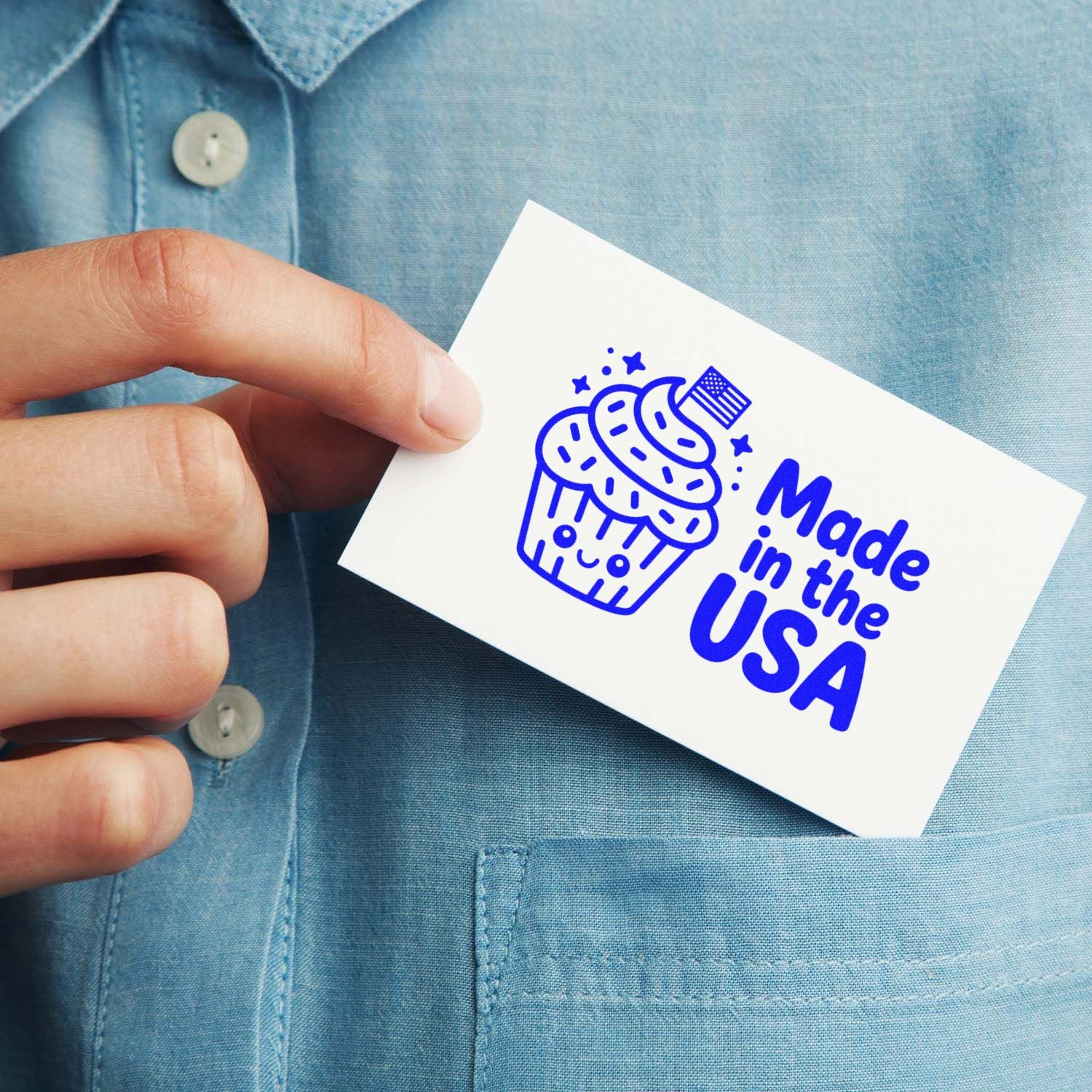 Hand holds a white card with a blue Made in the USA cupcake stamp seal on a light blue shirt.