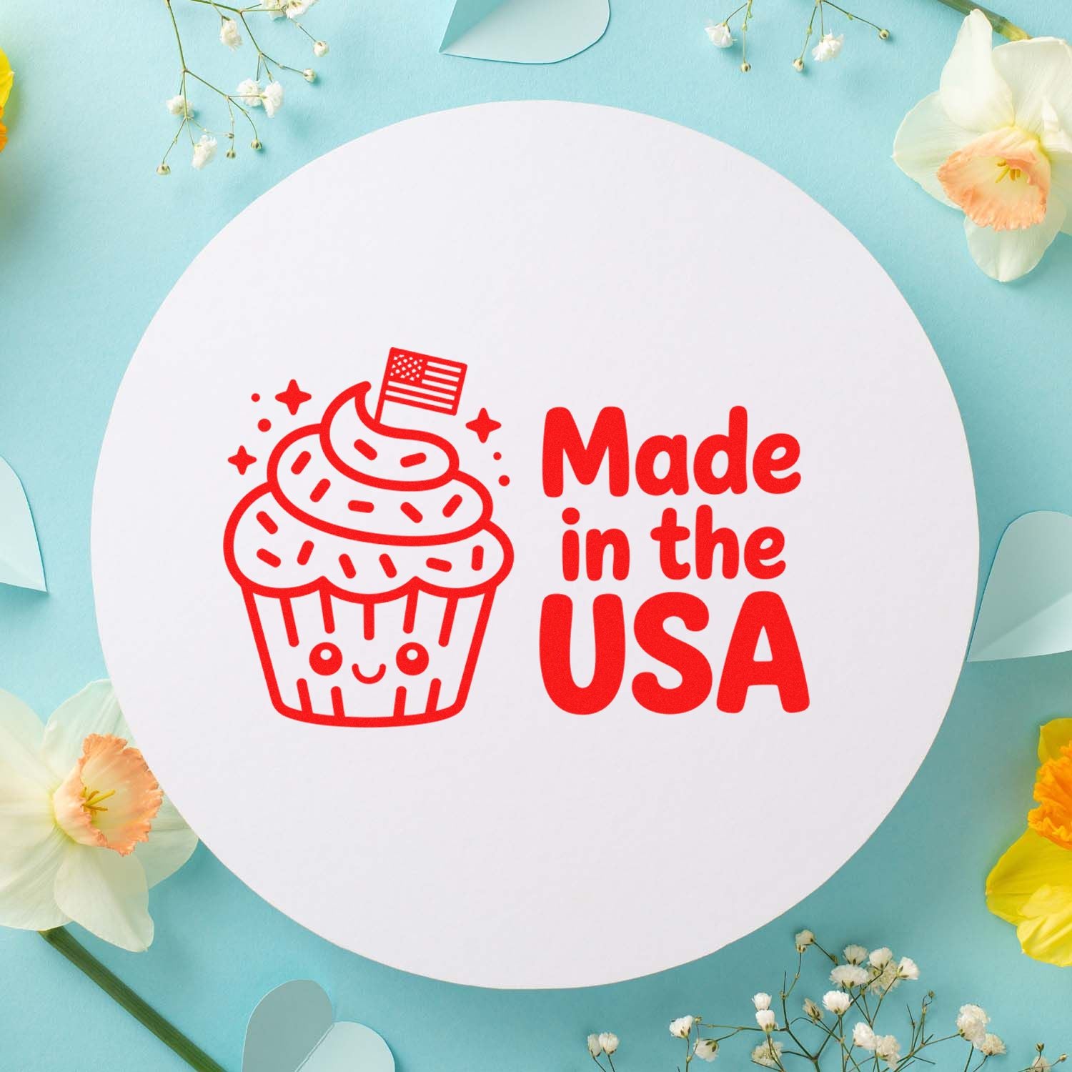 Red Made in the USA cupcake stamp on a white round seal, set against a pastel blue floral background.