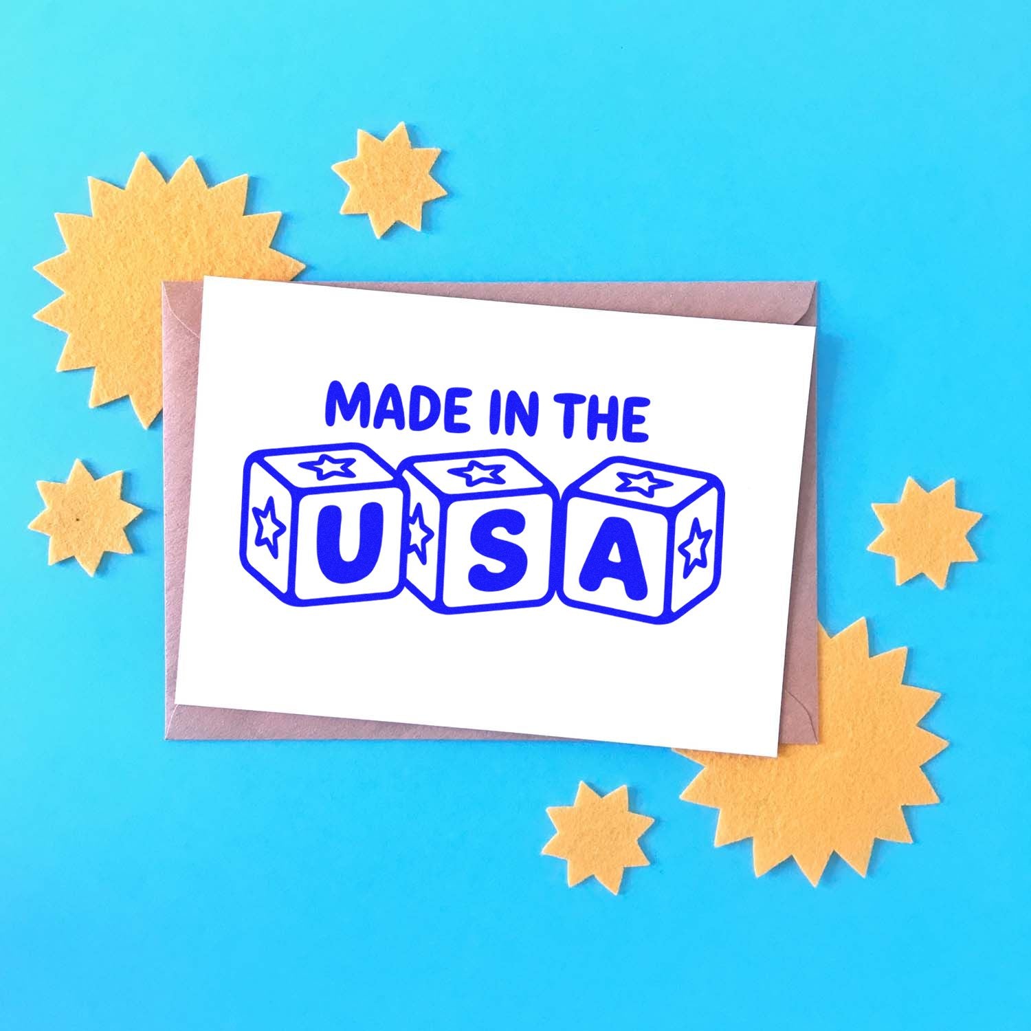 Blue Made in the USA stamp seal on white card with pink envelope, on turquoise background with yellow starburst accents.