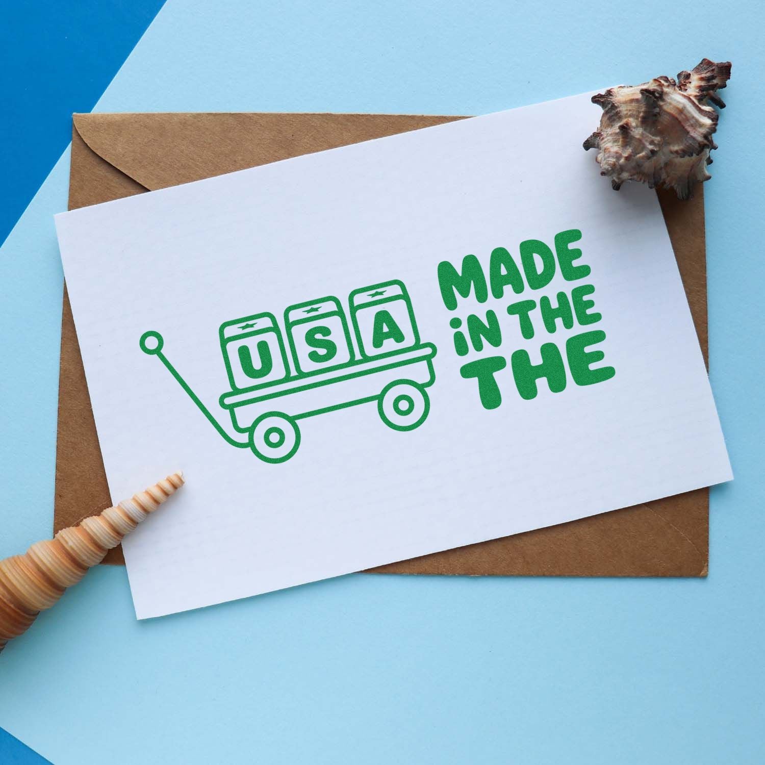 Green USA-made stamp seal on white card over kraft envelope, with seashell accents on a light blue background.