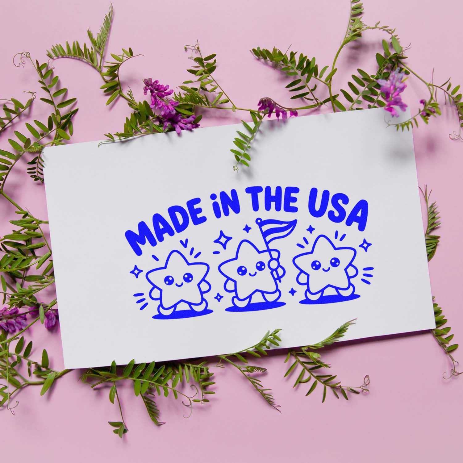 Blue Made in the USA stamp and seal design with cute stars on white card, framed by green vines and purple flowers on pink background