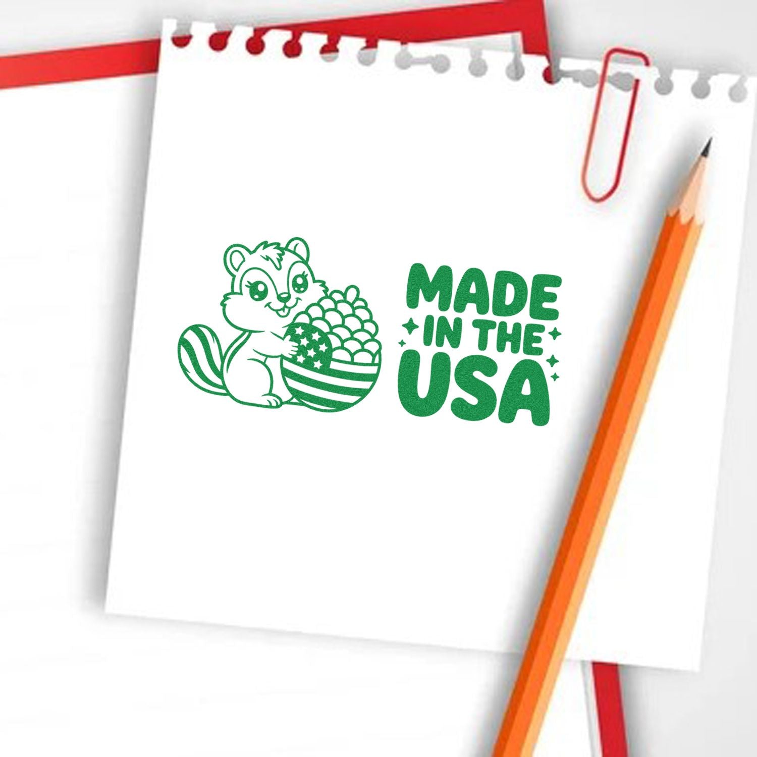 Green Made in the USA stamp seal with squirrel holding patriotic acorn on white notepad, beside orange pencil.