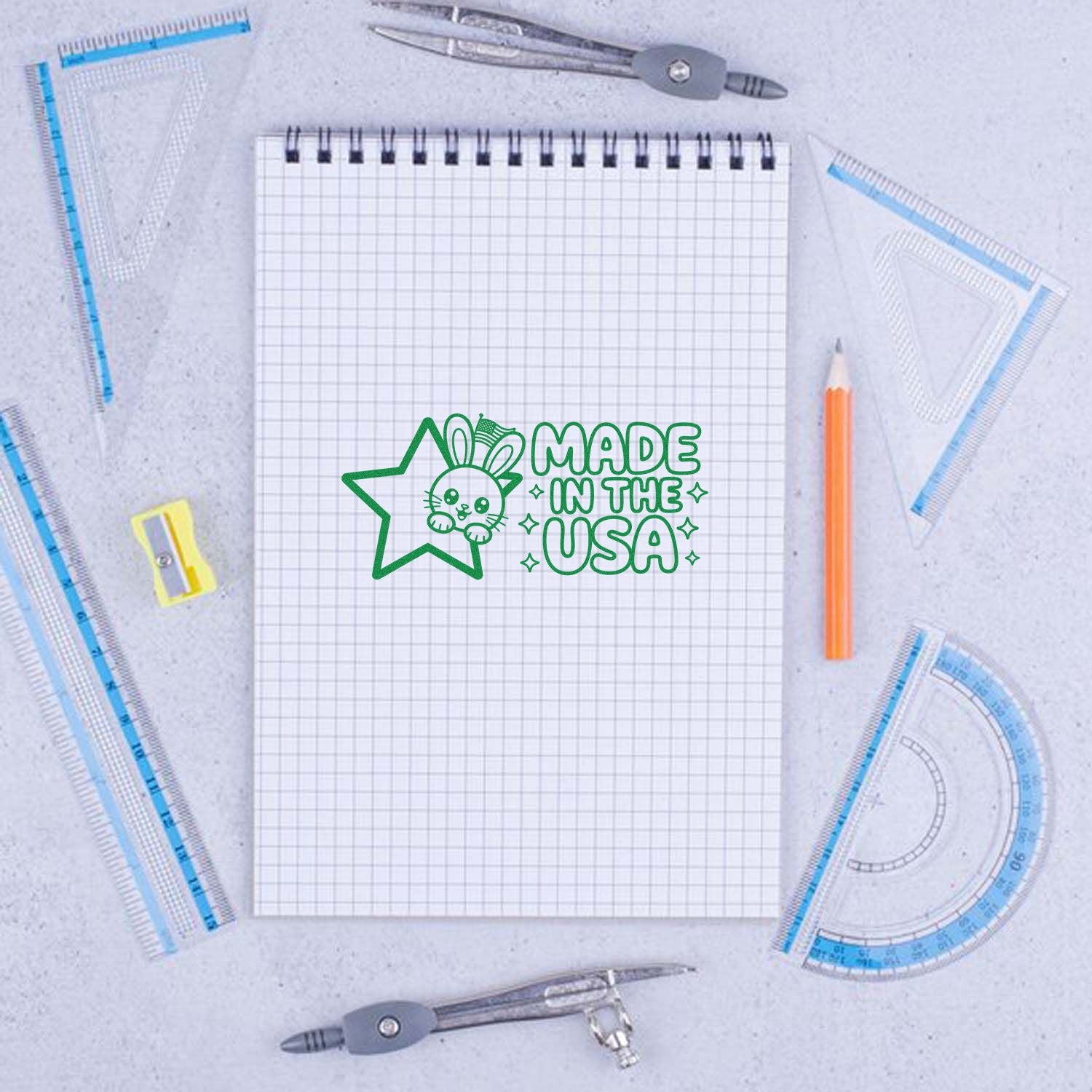 Green custom stamp and seal with bunny and Made in the USA on graph notebook, surrounded by drafting tools.