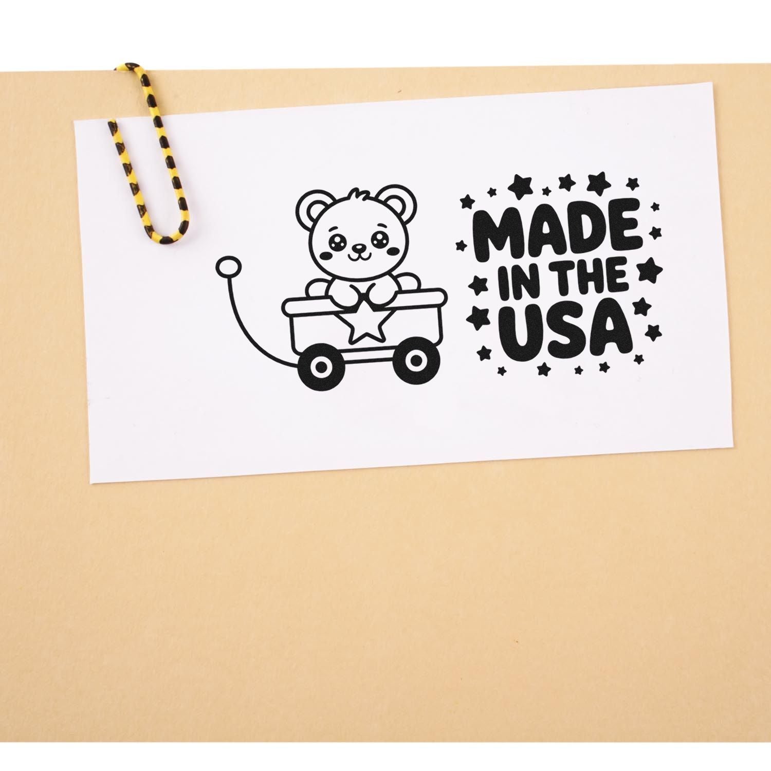 Black stamp seal with bear in wagon and MADE IN THE USA text, clipped to tan paper with yellow-black cord.