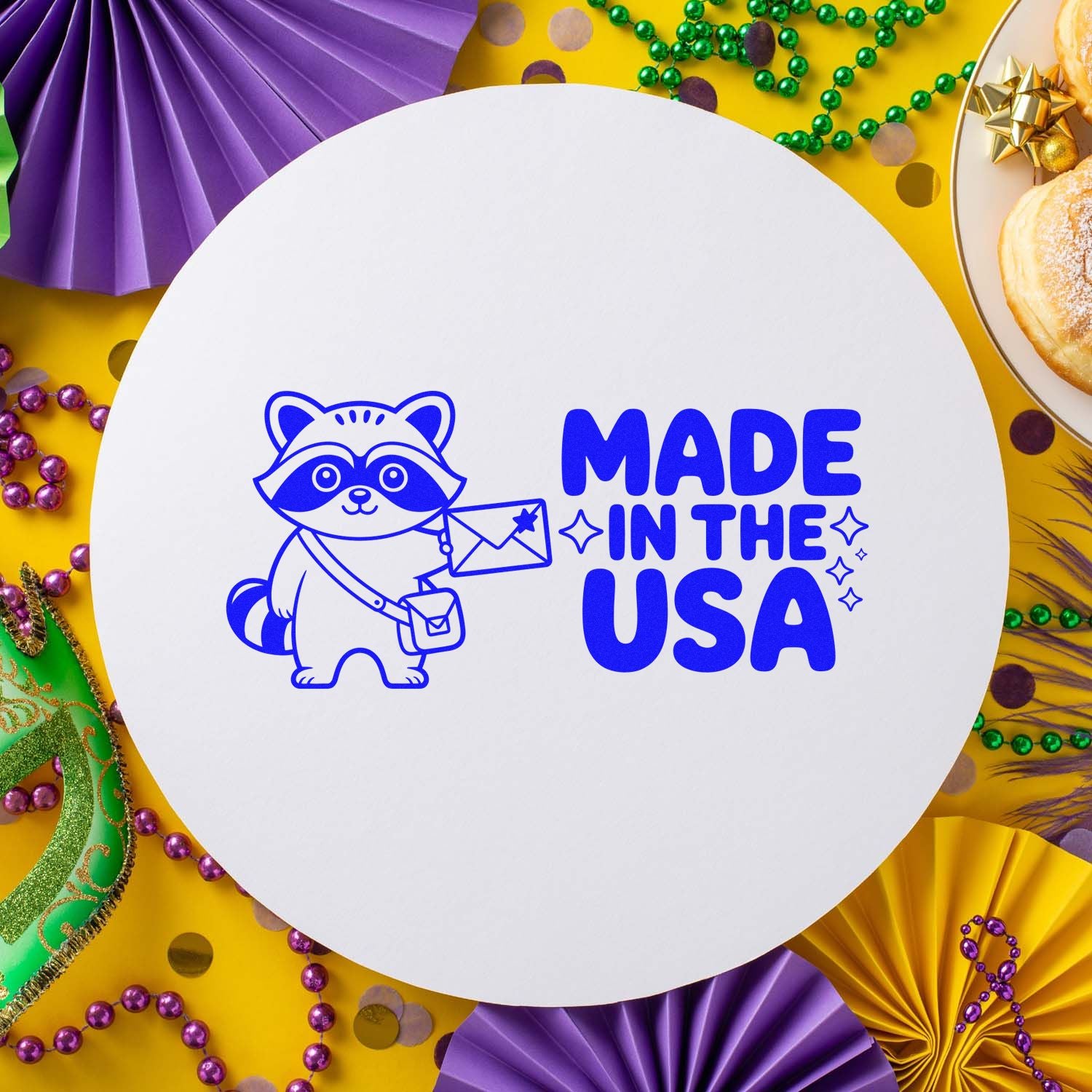 White round stamp seal with blue raccoon and Made in the USA text on a yellow Mardi Gras backdrop with beads and purple accents.