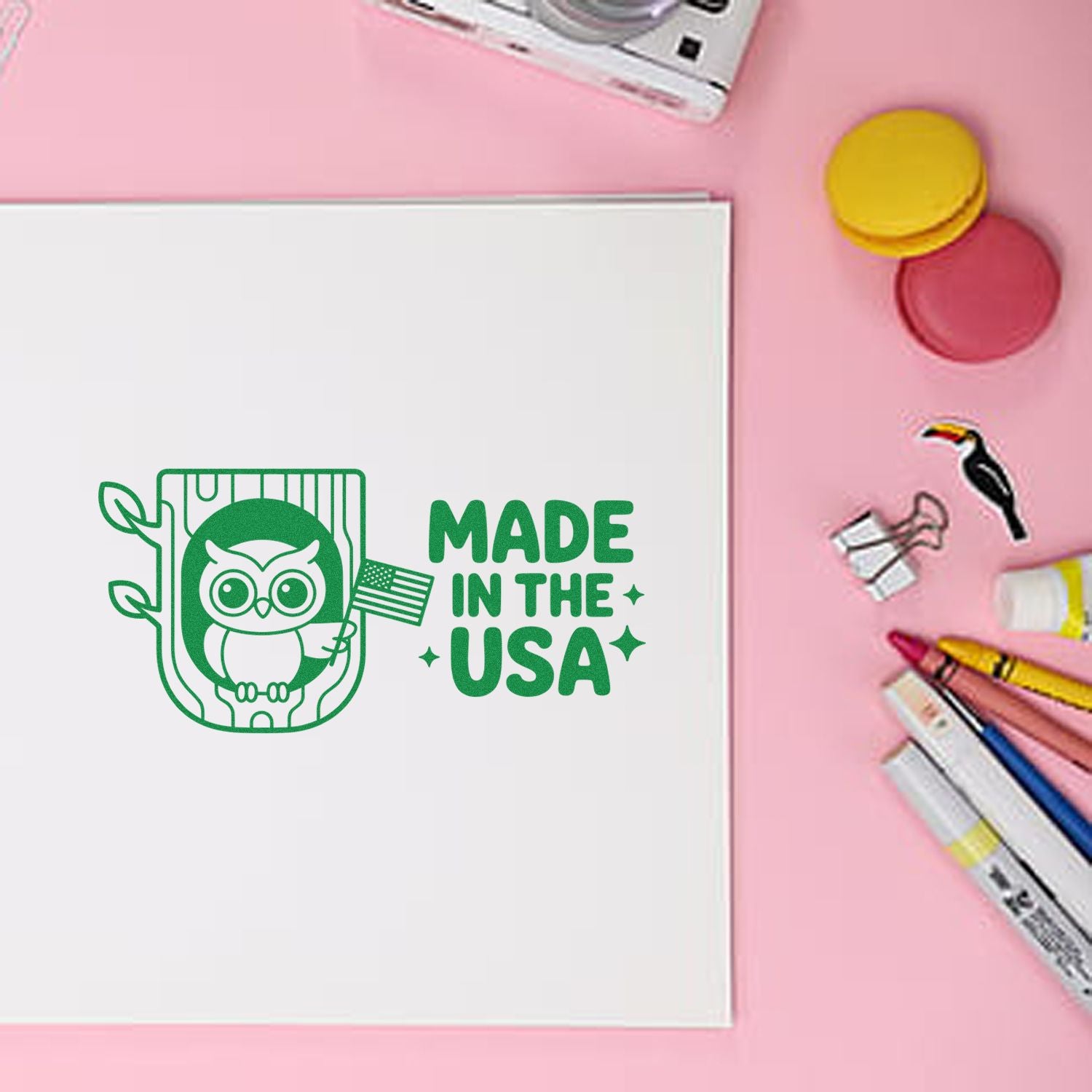 Green Made in the USA stamp with owl icon on white paper, surrounded by colorful stamp and seal supplies on a pink background.