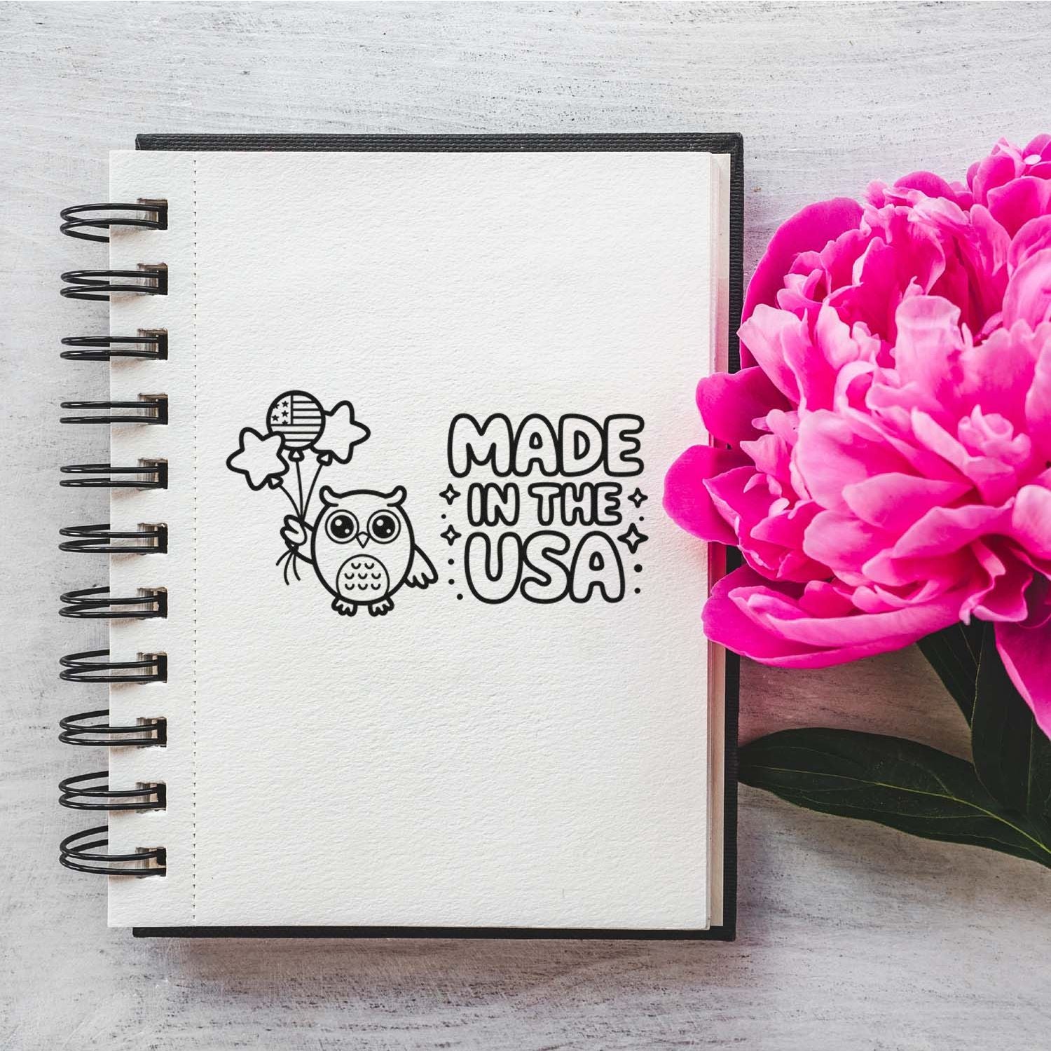 Notebook with black Made in the USA owl stamp seal, bright pink peonies, and spiral binding.