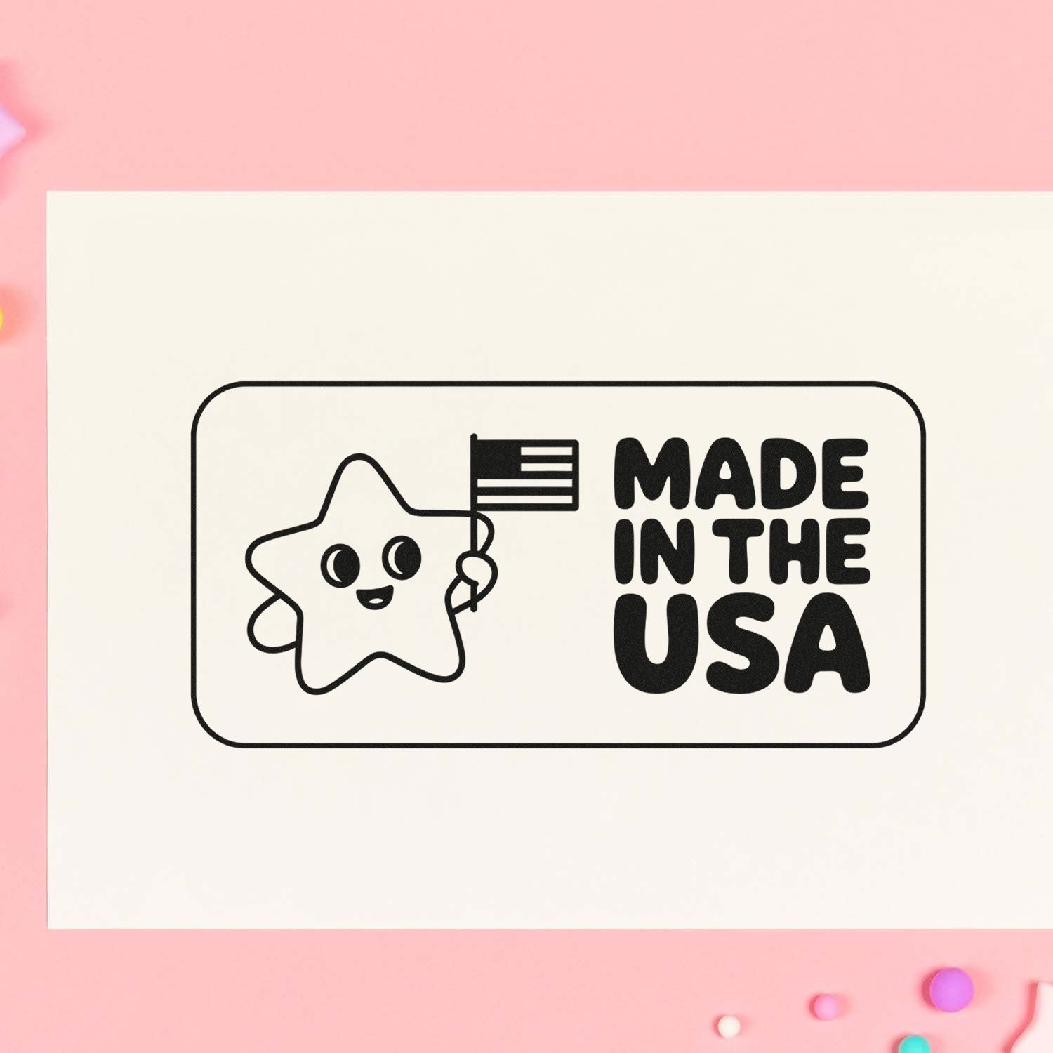 Black Made in the USA stamp seal with smiling star holding an American flag on a cream card over a pink background.