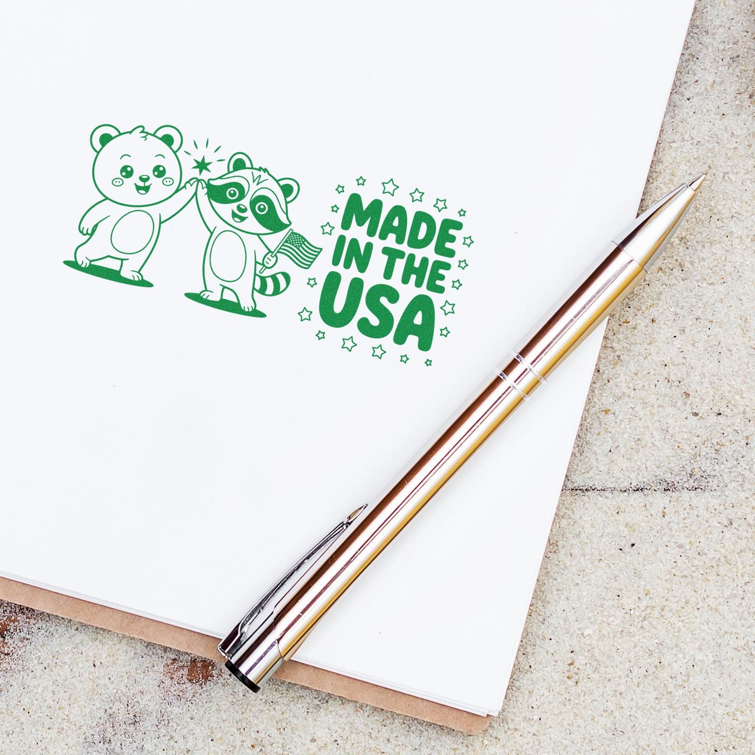 Green custom stamp seal with bear and raccoon, Made in the USA text, on white paper beside a gold pen.