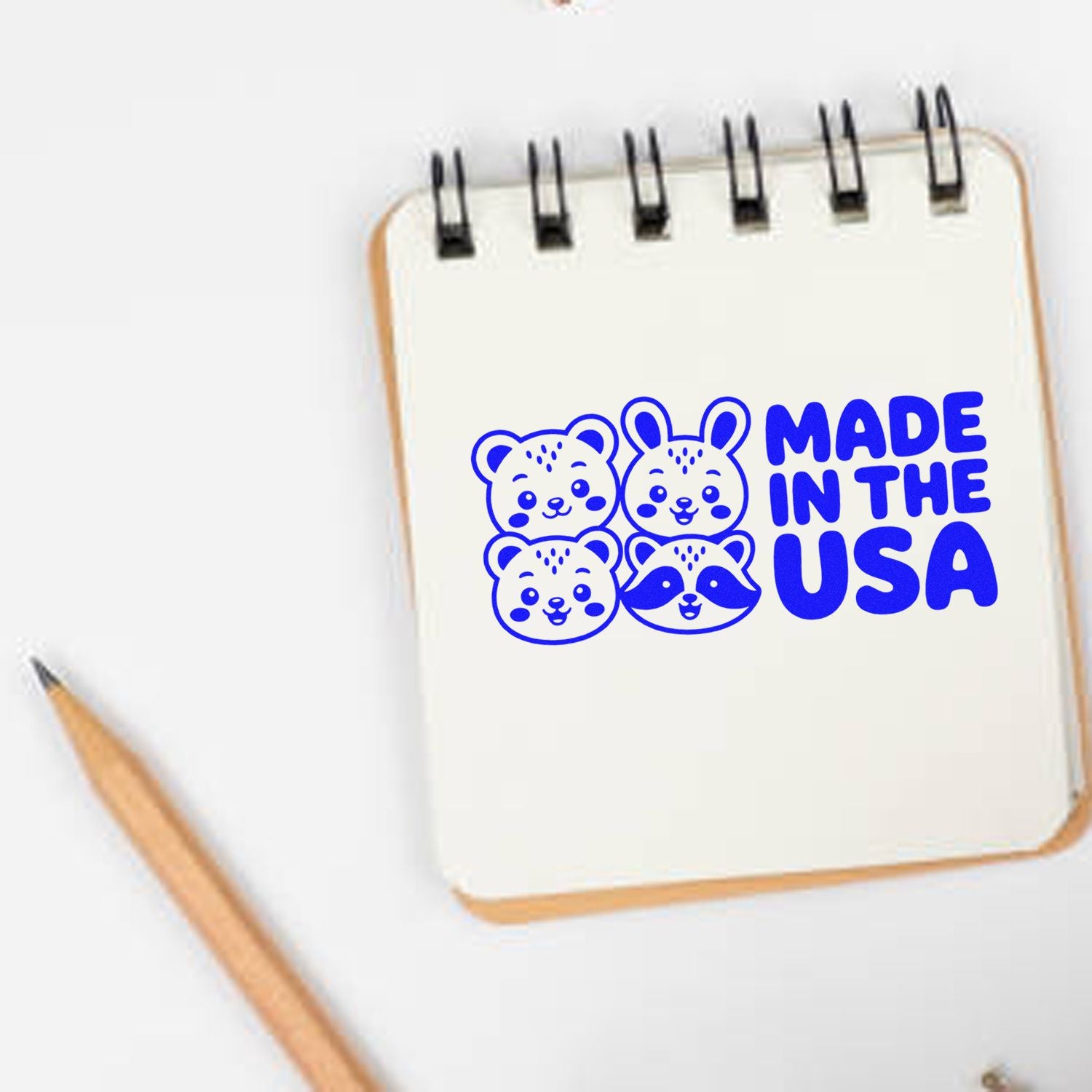 Blue "Made in the USA" stamp on spiral notepad with bear, bunny, and raccoon faces, beside a pencil.