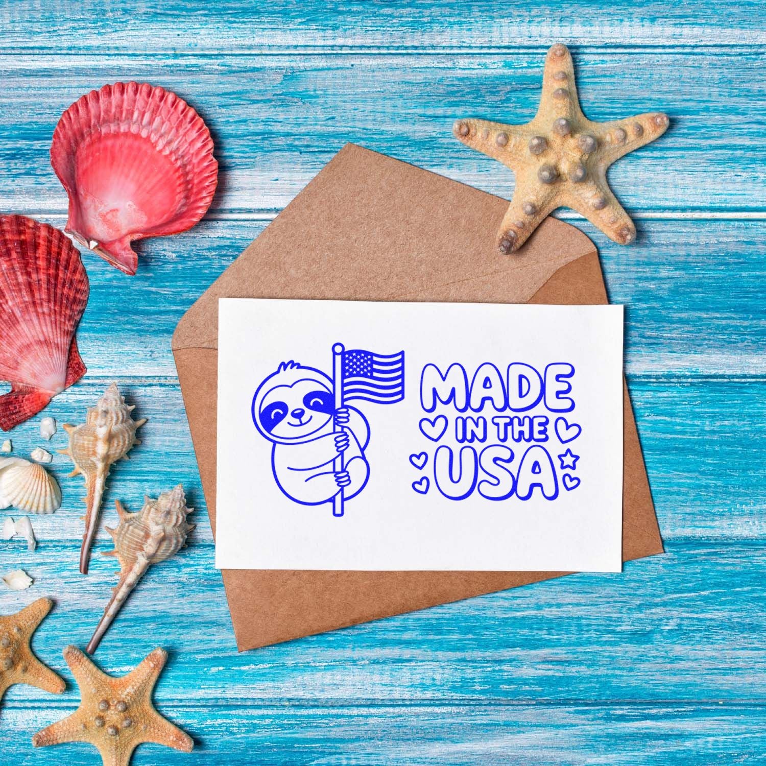 Blue Made in the USA stamp and seal on white card over kraft envelope, with seashells and starfish on turquoise wood.