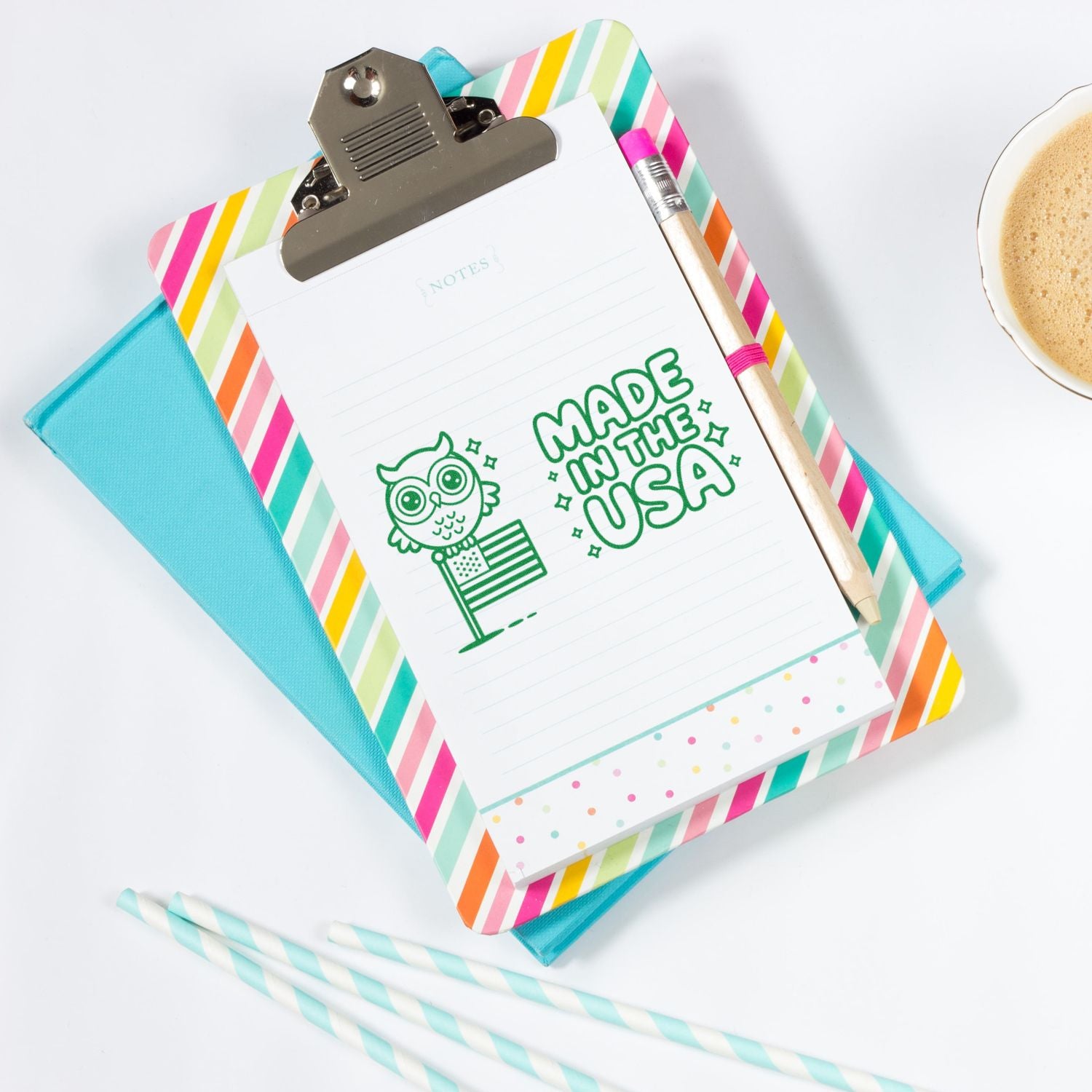 Green owl and Made in the USA stamp on a striped clipboard with pastel notepad, turquoise folder, pencil, and coffee cup.