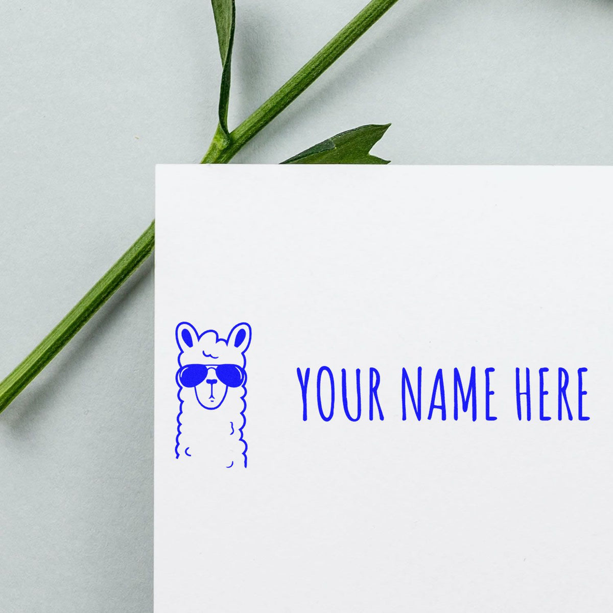 Blue custom llama stamp and seal with sunglasses and YOUR NAME HERE on a white card, with green stem on a light gray background.