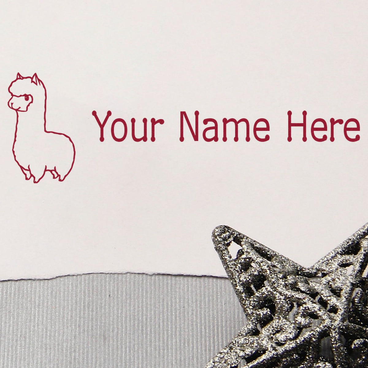 Red llama name stamp with Your Name Here text and silver glitter star seal on white paper.