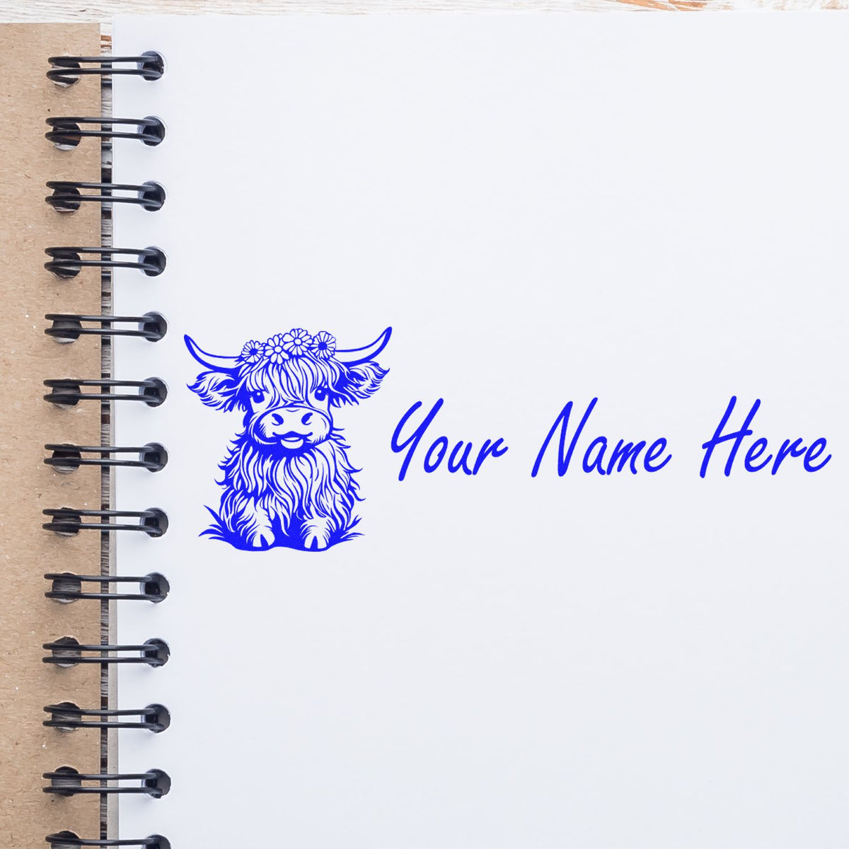 Blue custom stamp seal with a floral cow and Your Name Here on a white spiral notebook page.