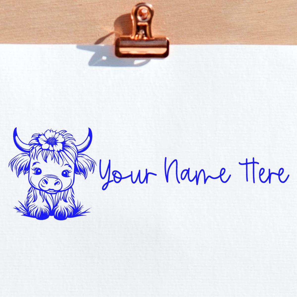 Blue custom stamp seal with cute cow illustration and Your Name Here on white paper, clipped with a copper binder clip.