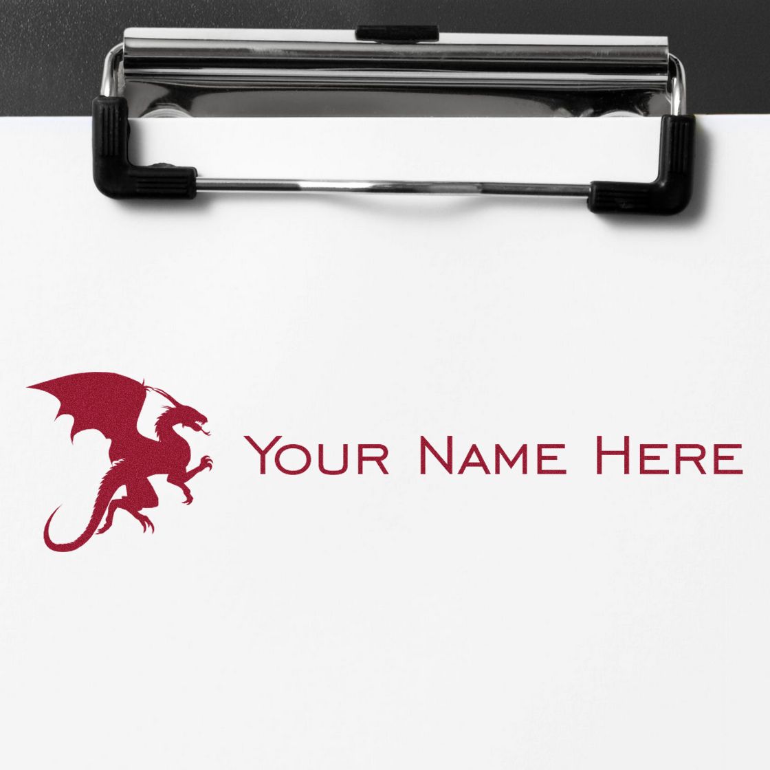 Custom stamp and seal sample with red dragon logo and Your Name Here on white paper, clipped by a chrome clipboard.